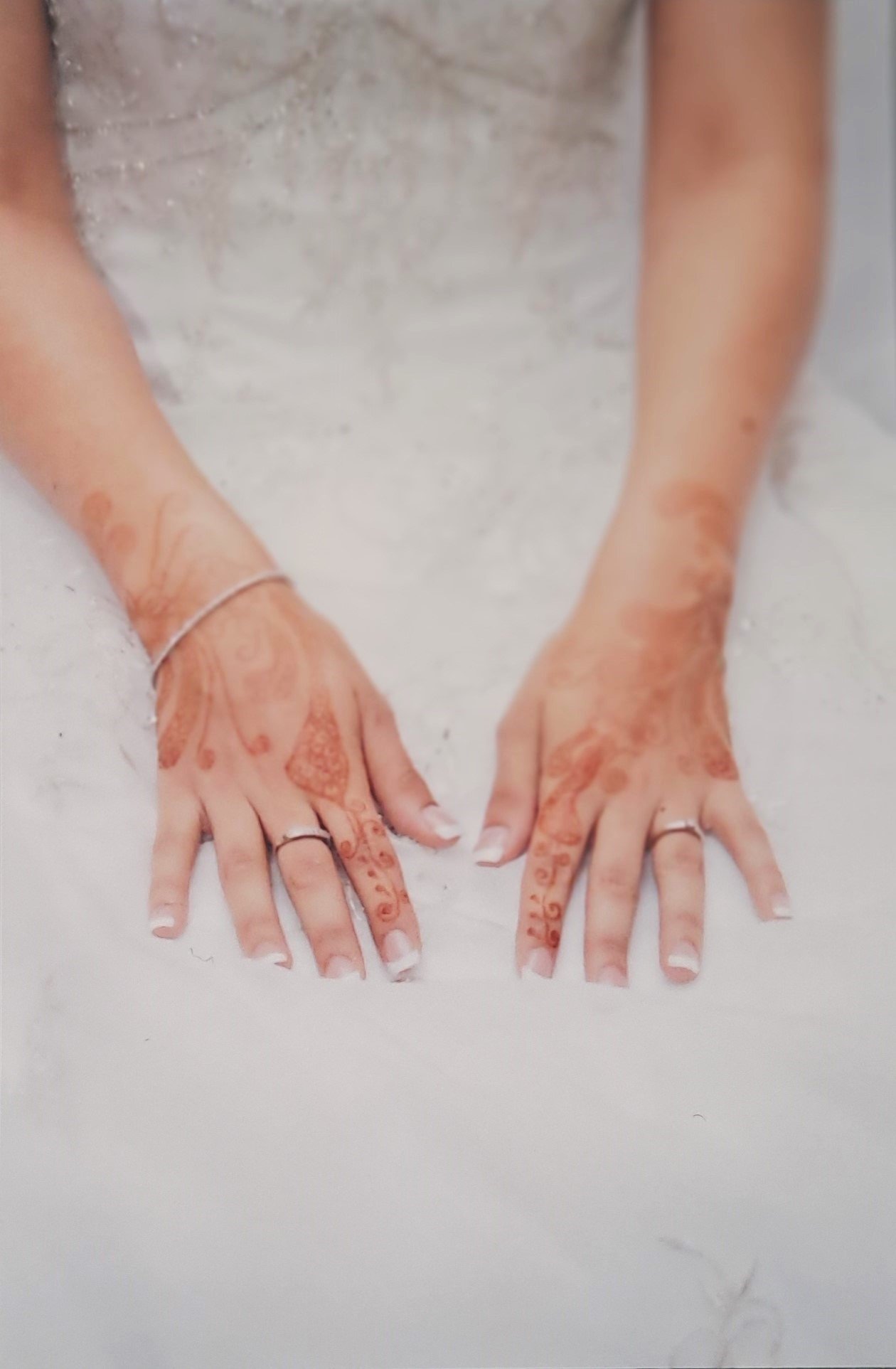 Mains d'une personne portant des bijoux et des tatouages, posées sur une surface blanche, probablement dans un cadre de mariage ou de cérémonie.
