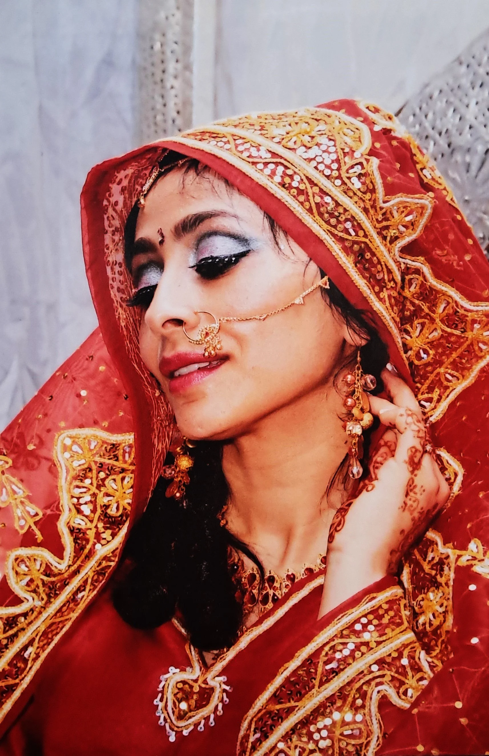 Femme portant une robe et un voile rouges, ornés de broderies dorées, avec des bijoux traditionnels indiens, visage maquillé, yeux fermés, exprime la grâce et la célébration.