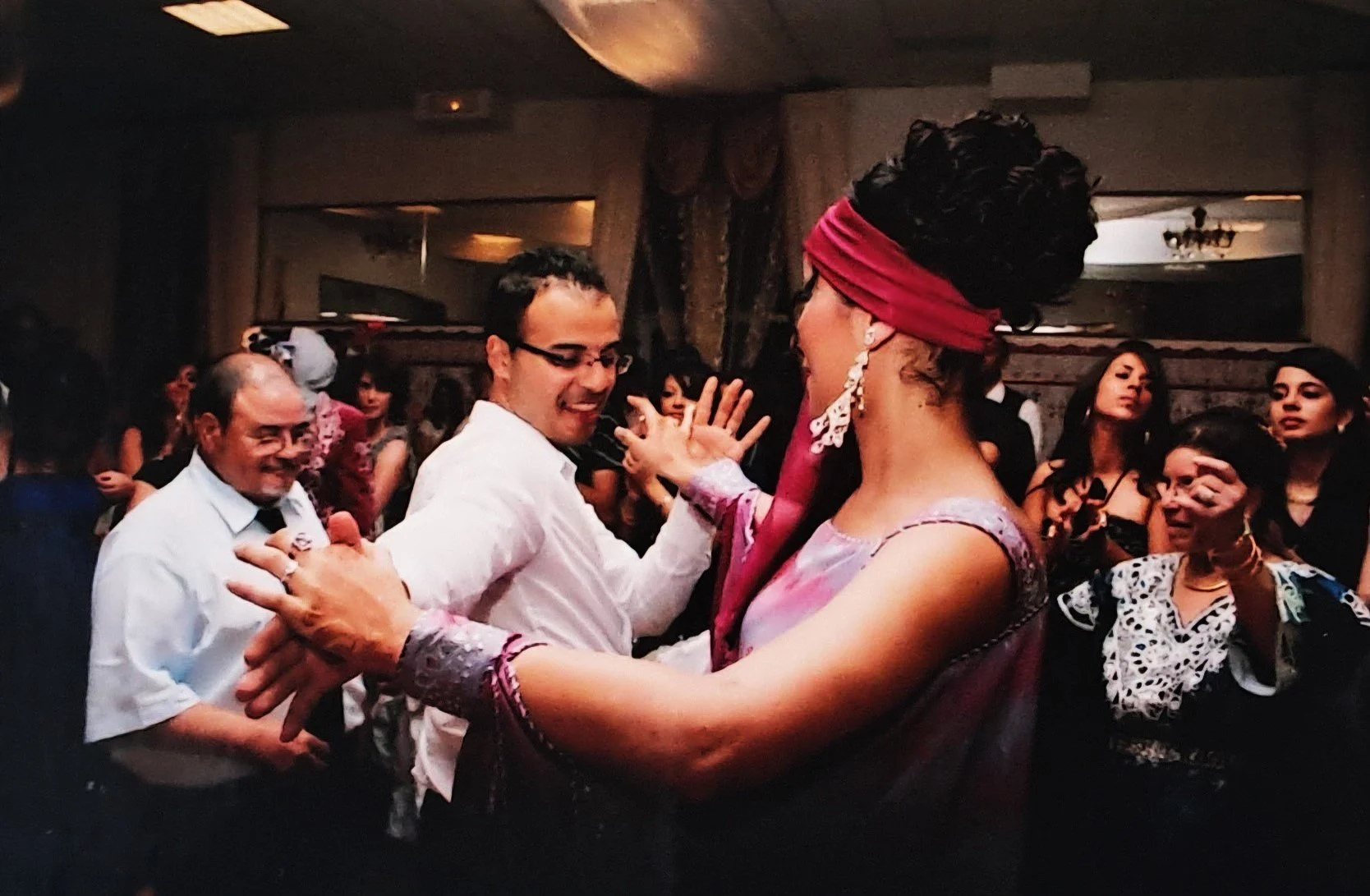 Groupe de personnes dansant lors d'une fête ou d'un mariage, avec un homme et une femme en premier plan dansant ensemble.