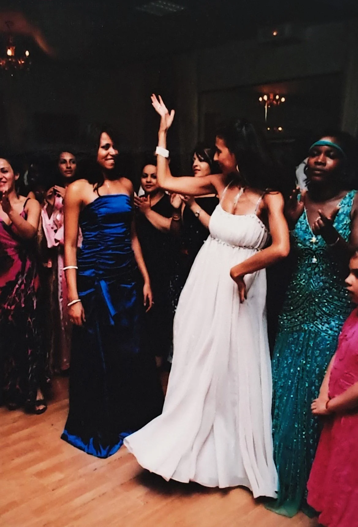 Fête dansante avec des femmes portant des robes colorées, deux femmes au centre dansent et s'amusent.