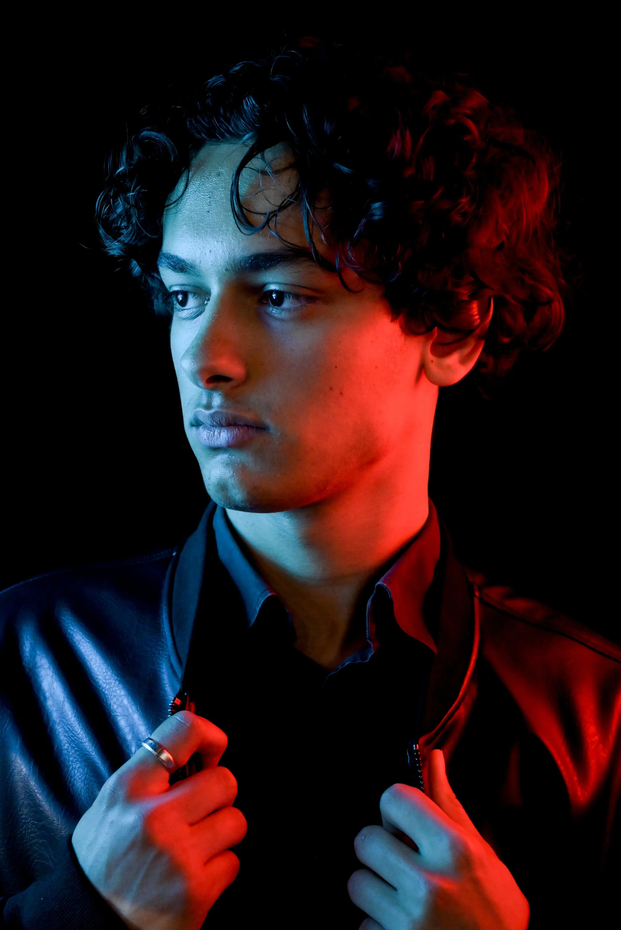 	

Un mannequin aux cheveux bouclés portant une veste en cuir, éclairé en lumière bleue et rouge, regardant vers la gauche, contre un fond noir, dans les studio photo de TF1 Mode, Malakoff pour Icastt 