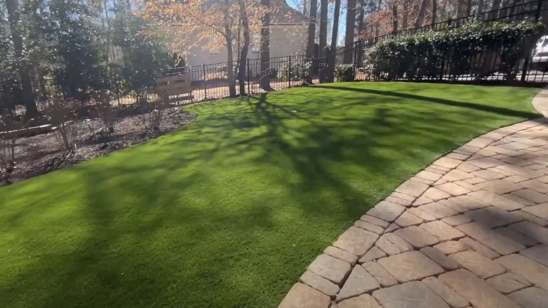A backyard with a green lawn, stone pathway, and surrounding trees and shrubs.