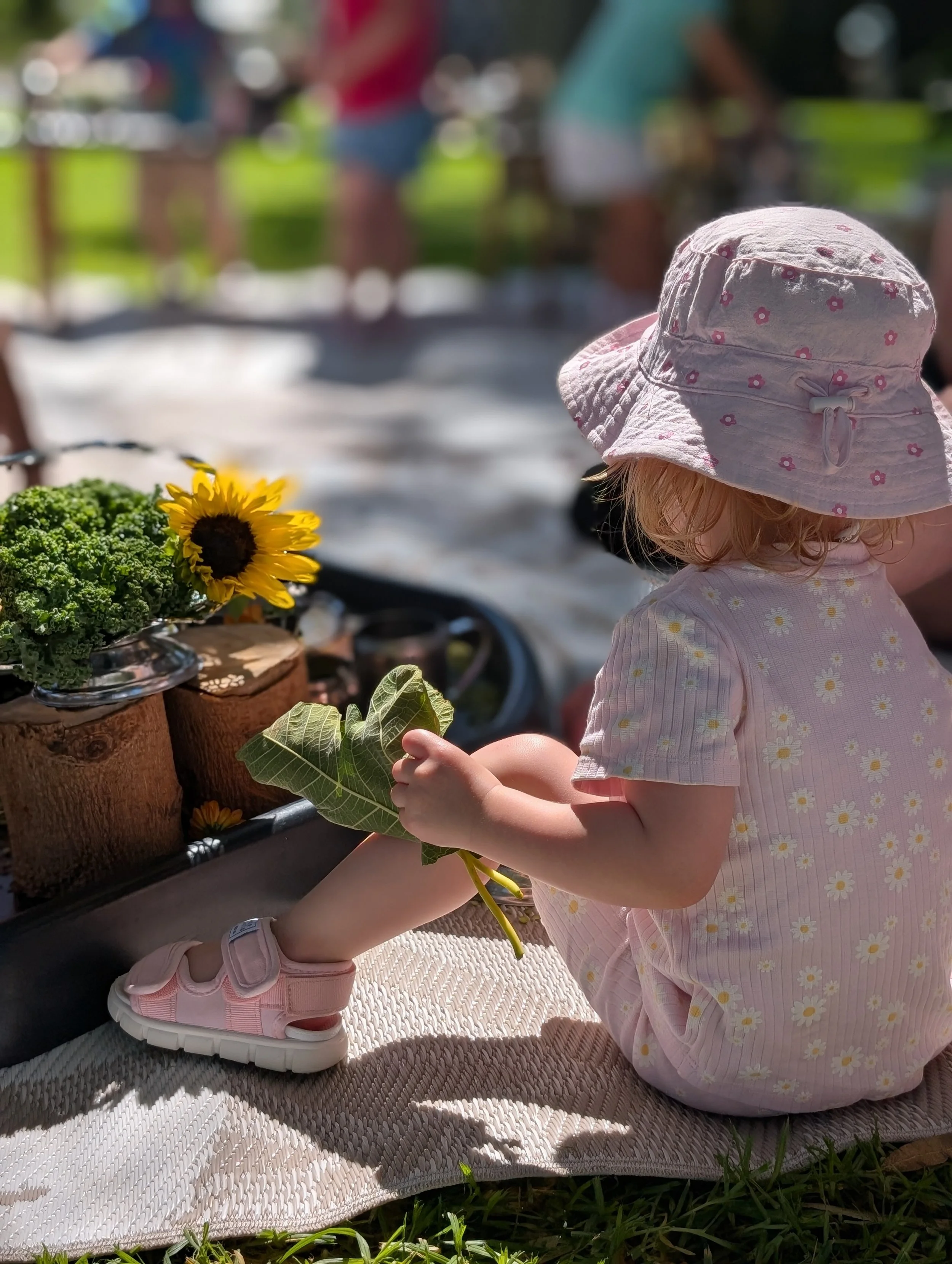 toddler outdoors in nature playing with messy play sensory tray with leaves and flowers
