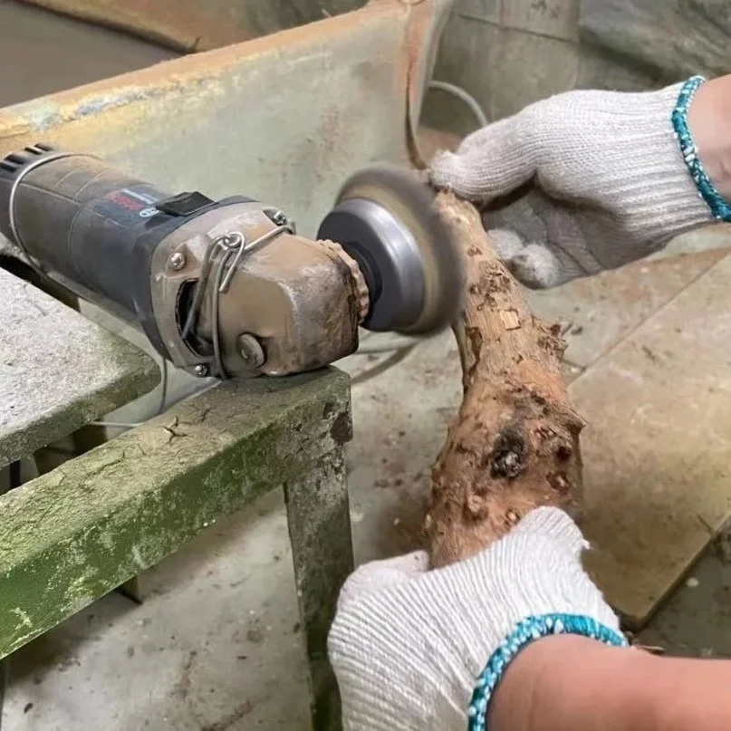Person wearing gloves uses a power rotary tool to carve or sand a piece of wood.