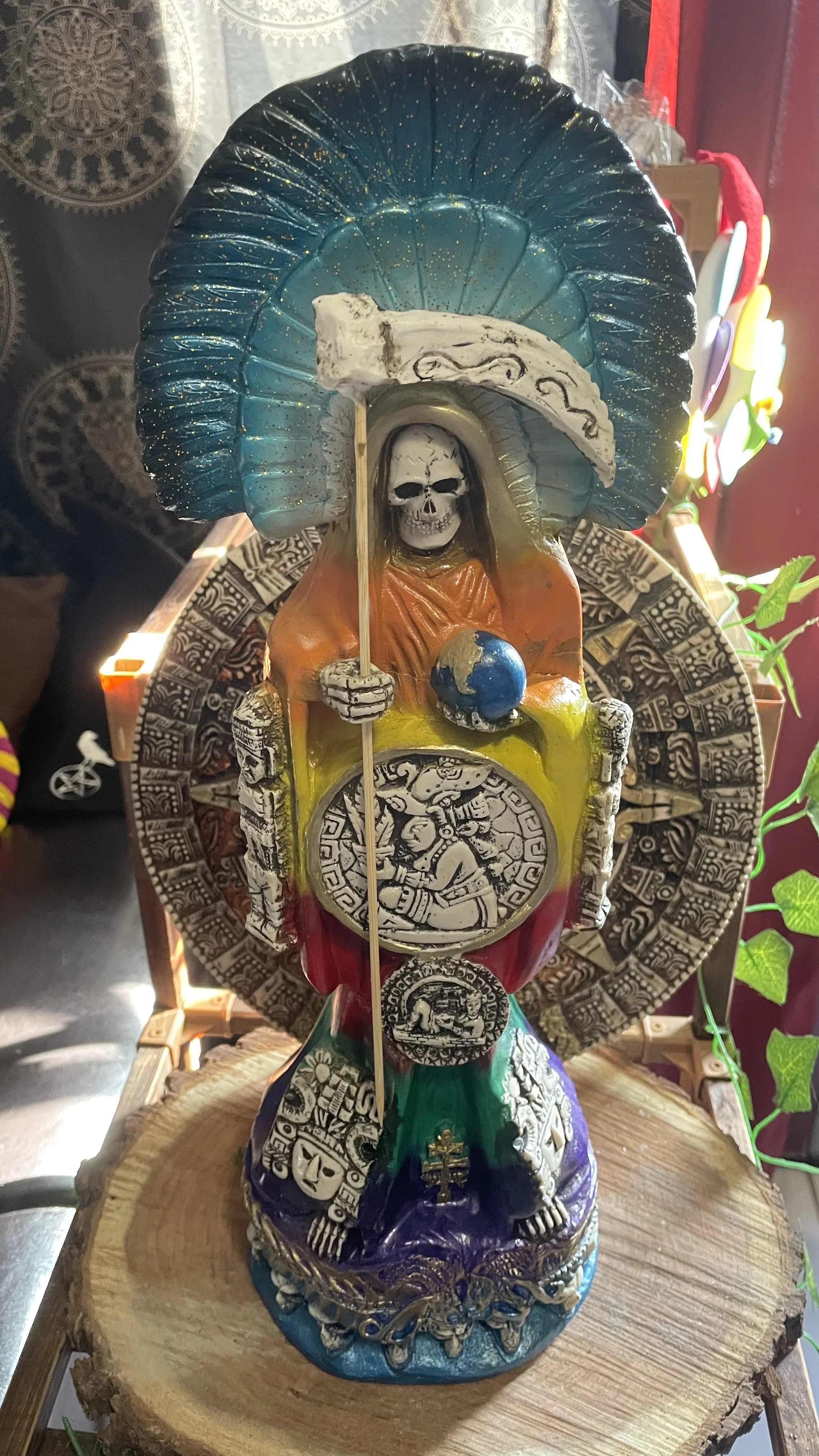 Colorful Santa Muerte statue with scythe and globe, featuring intricate designs and patterns, placed on a wooden surface.