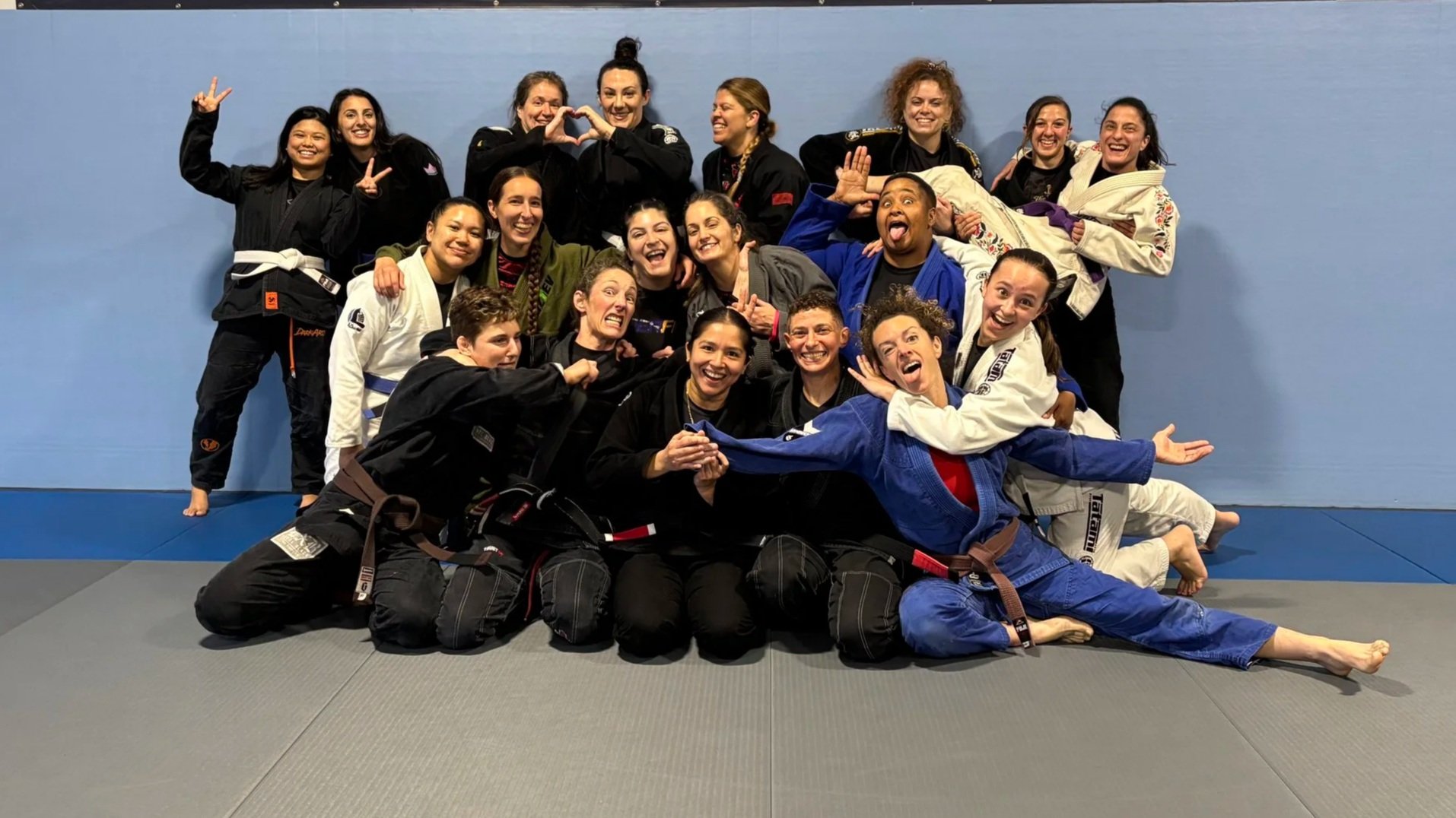 Two women in Brazilian Jiu-Jitsu gis smiling and posing together inside martial arts gym.