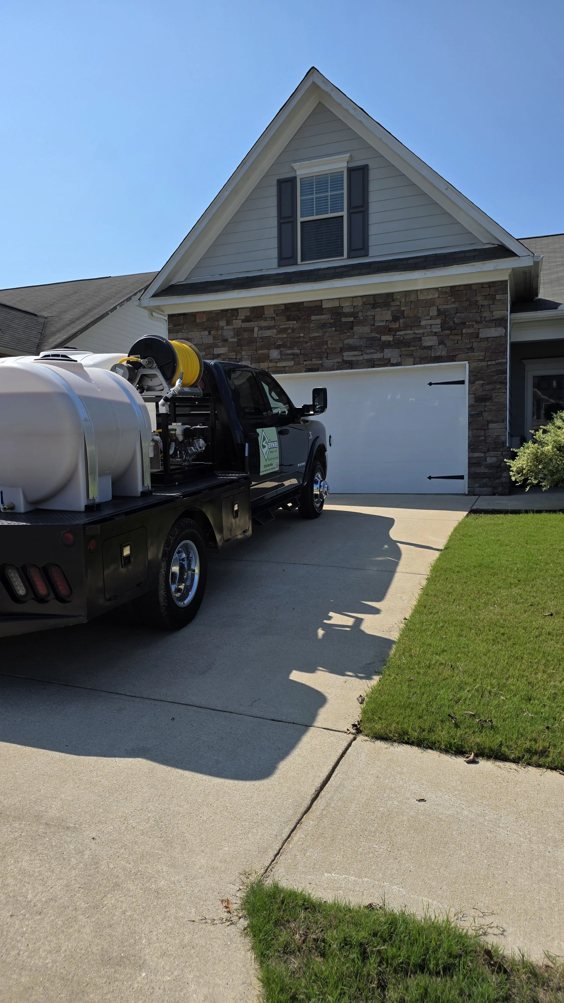A house with a stone and siding facade, a pitched roof, and a window with shutters. A black truck with pest control equipment is parked on the driveway.