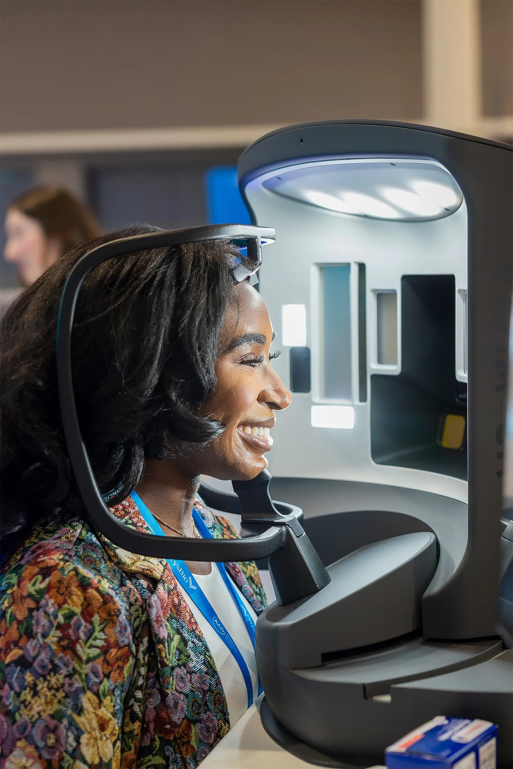 A woman smiling and looking through an eye examination device in a clinic or optometry office.