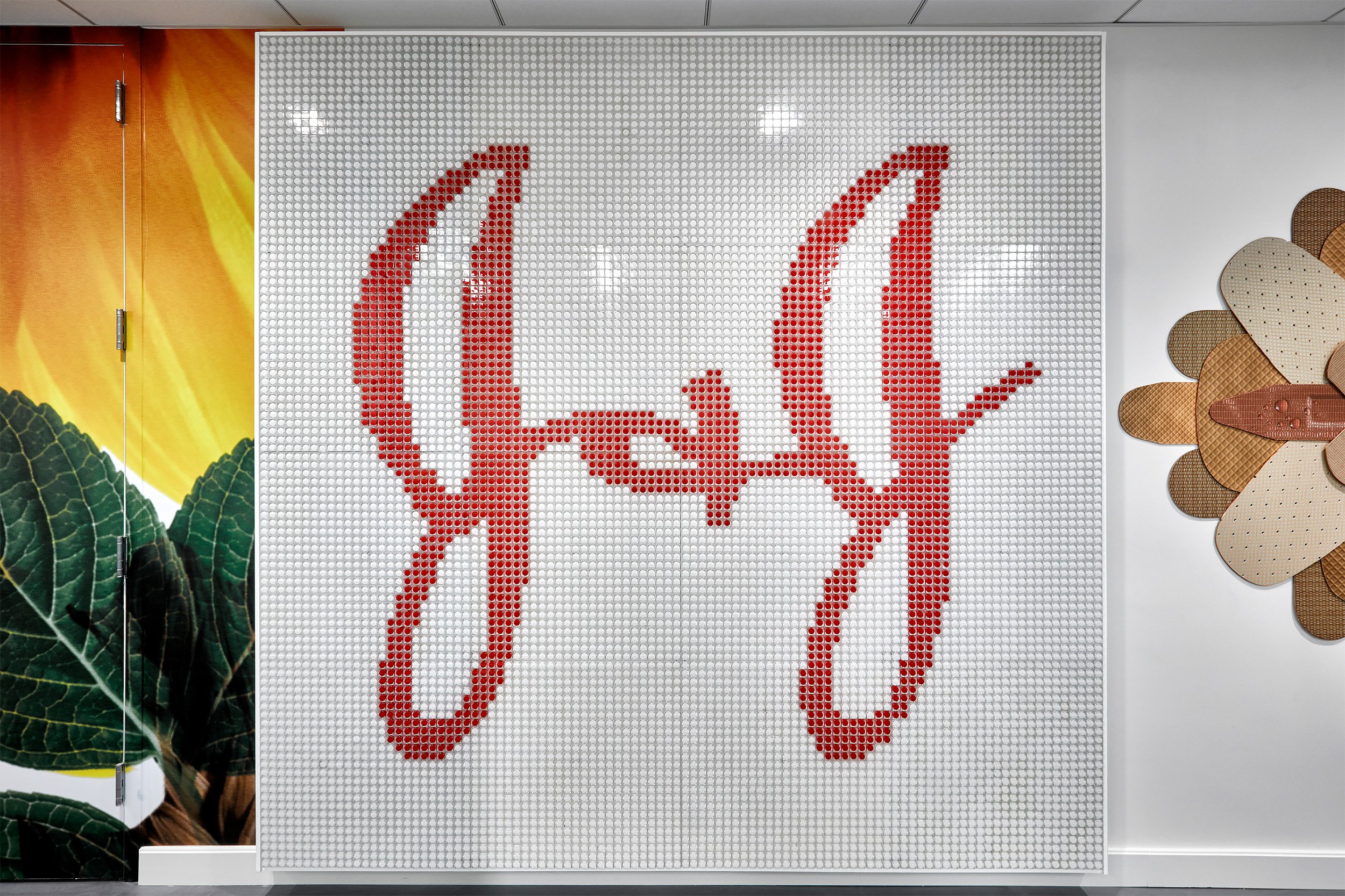 A decorative wall art piece made of small, round, white and red objects, forming a stylized signature or text.
