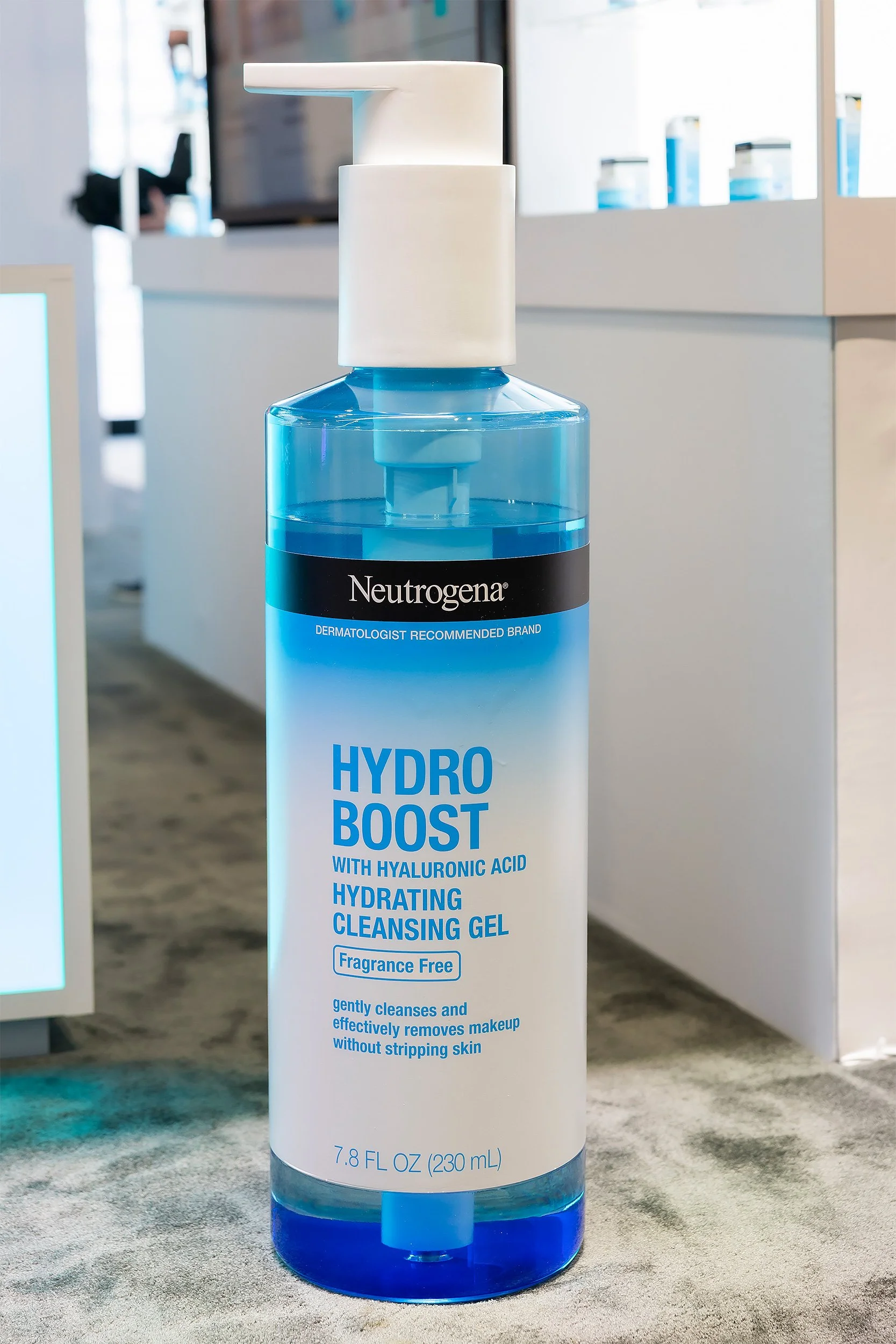 A large bottle of Neutrogena Hydro Boost cleansing gel with hyaluronic acid, fragrance-free, and hydrating properties, placed on a textured surface in a retail or display setting.