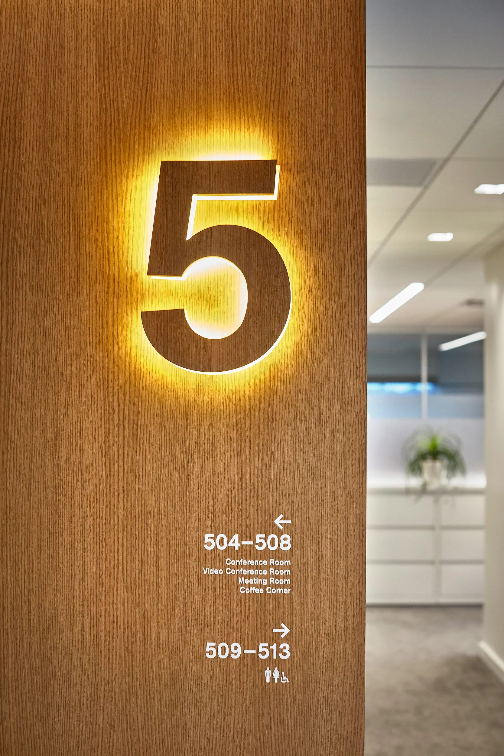Indoor hallway with a wooden sign displaying room numbers 504-508 and 509-513, with icons indicating restrooms and accessibility.