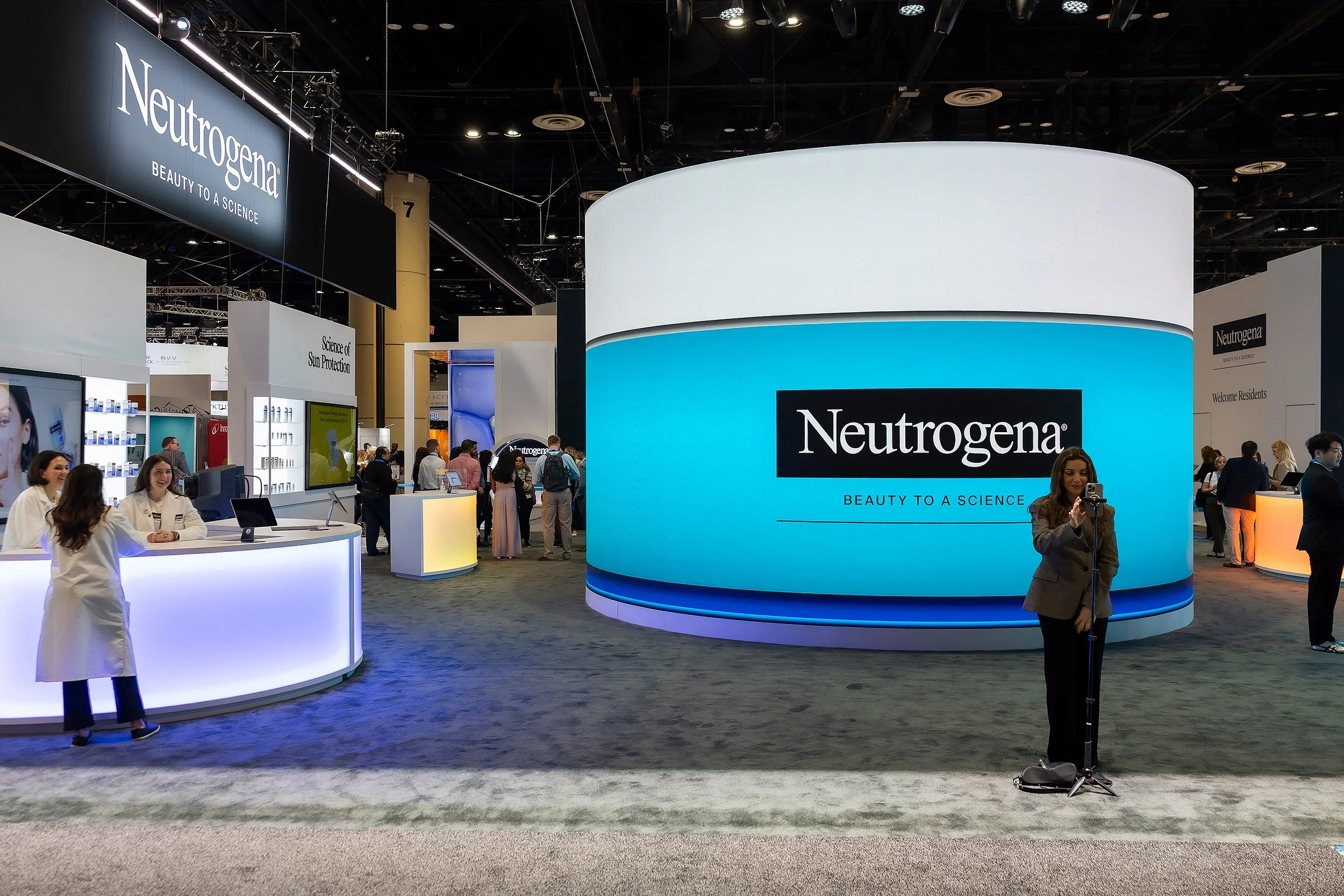 Trade show booth for Neutrogena with a large digital display and visitors walking around.
