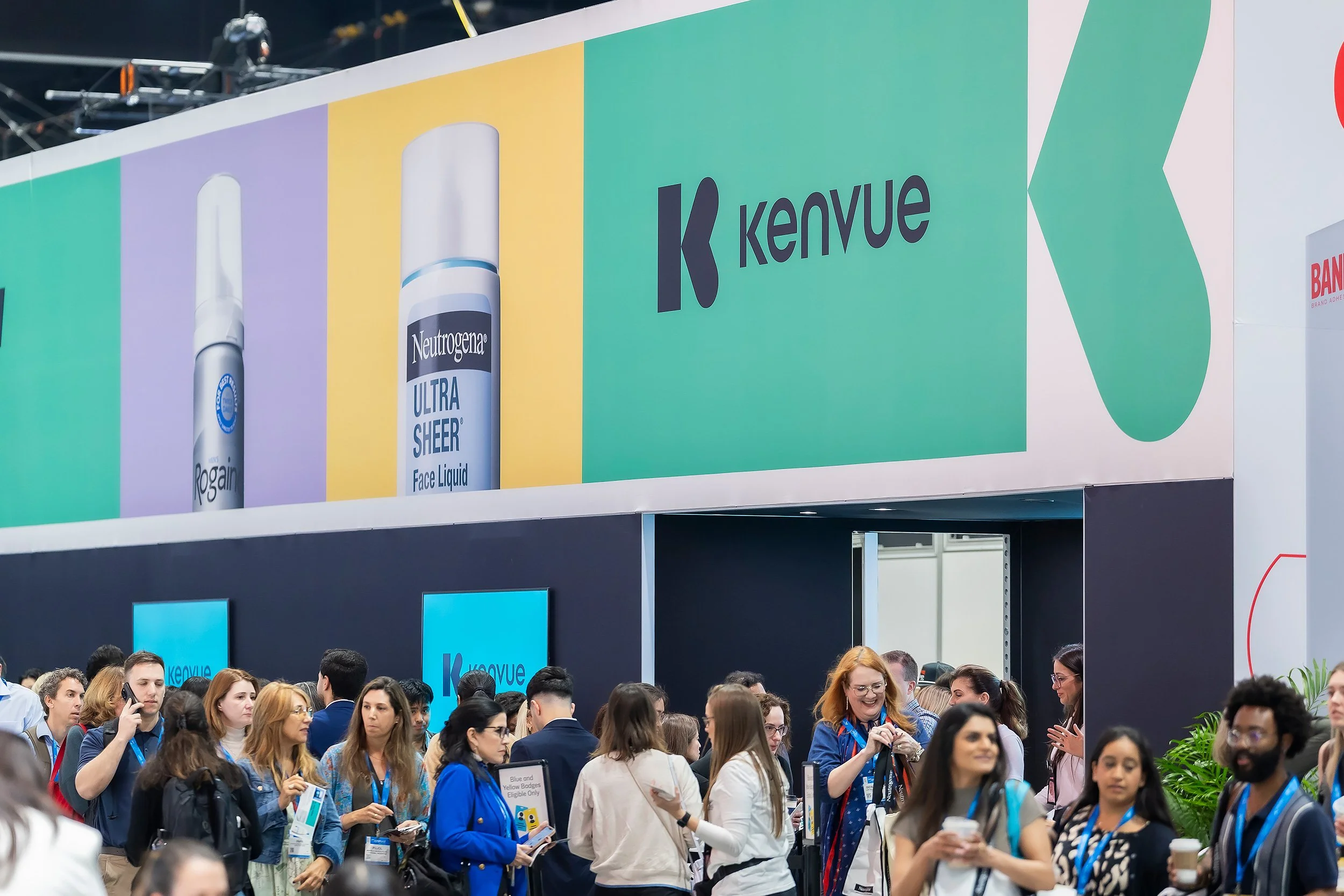 Crowd of people at a trade show or conference with Overhead banner displaying Kenvue logo and product images.