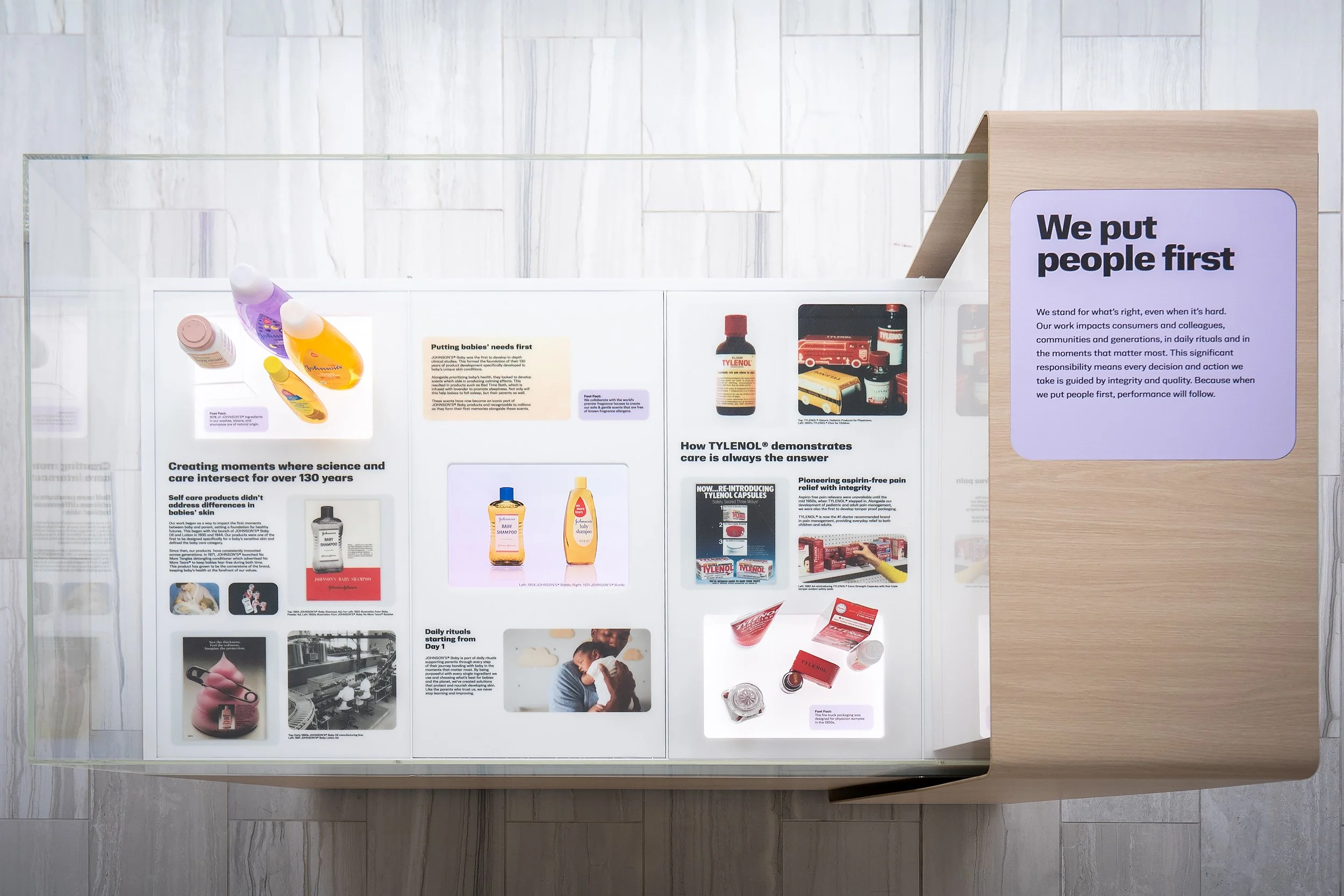 Display of informational posters and product samples within a glass case on a wooden stand, focusing on healthcare and consumer products.