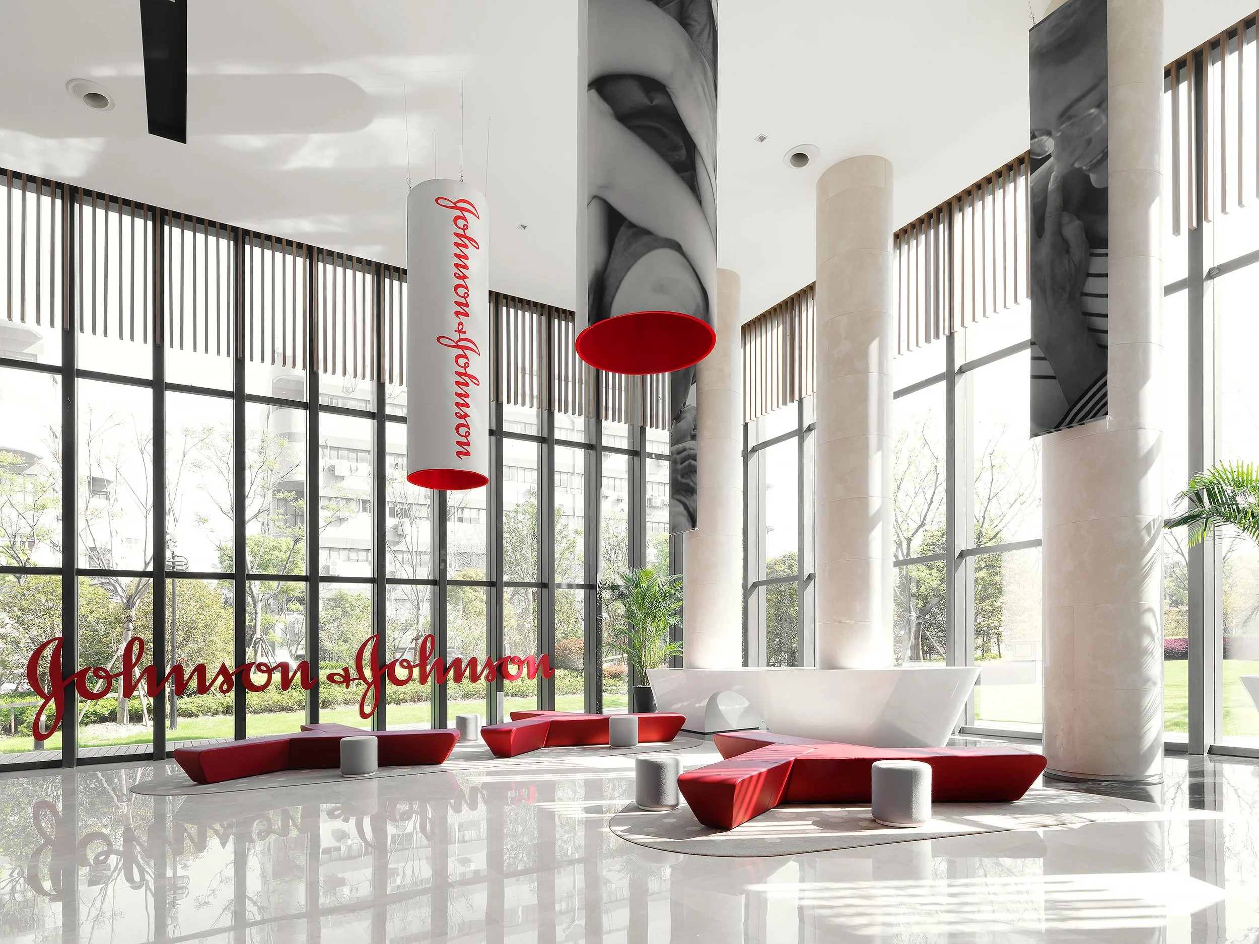 Modern, spacious interior with large glass windows, white and red furniture, a white bathtub, and a Johnson & Johnson sign.