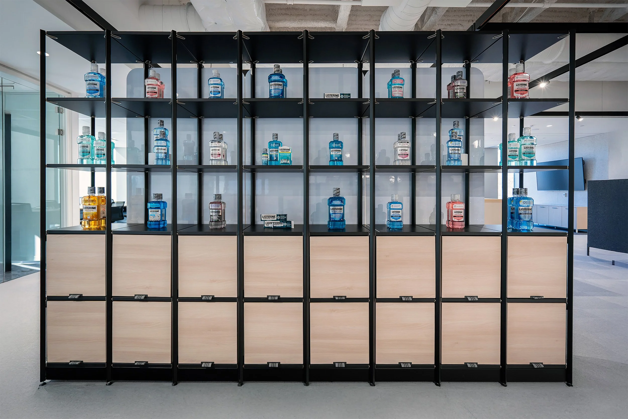 A black metal shelving unit with multiple compartments, containing bottles of Listerine mouthwash in various colors, placed in an indoor space with a modern, minimalist design.