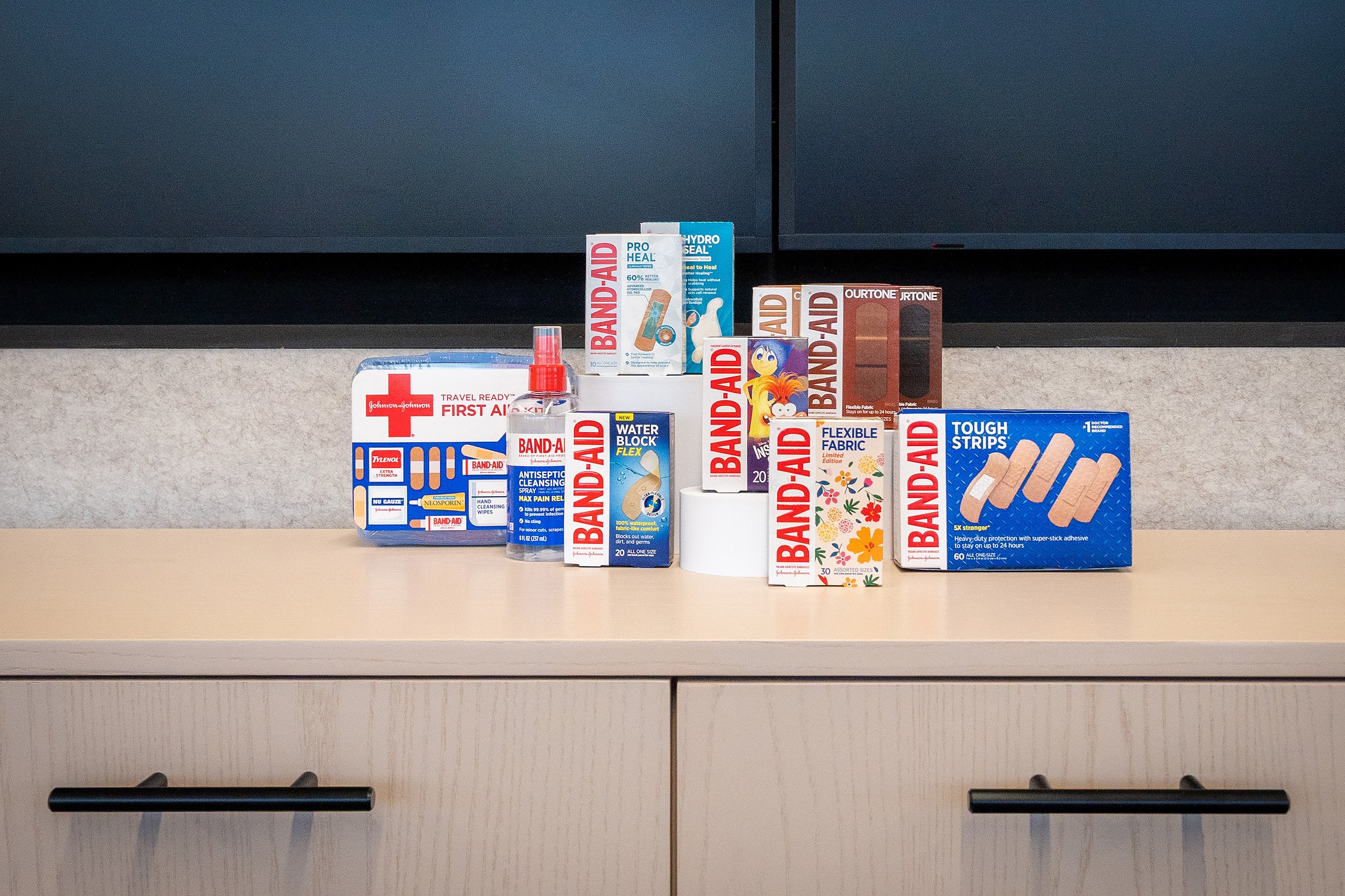 Assorted first aid and medical supplies on a beige shelf, including bandages, antiseptic spray, adhesive tape, and other wound care products.