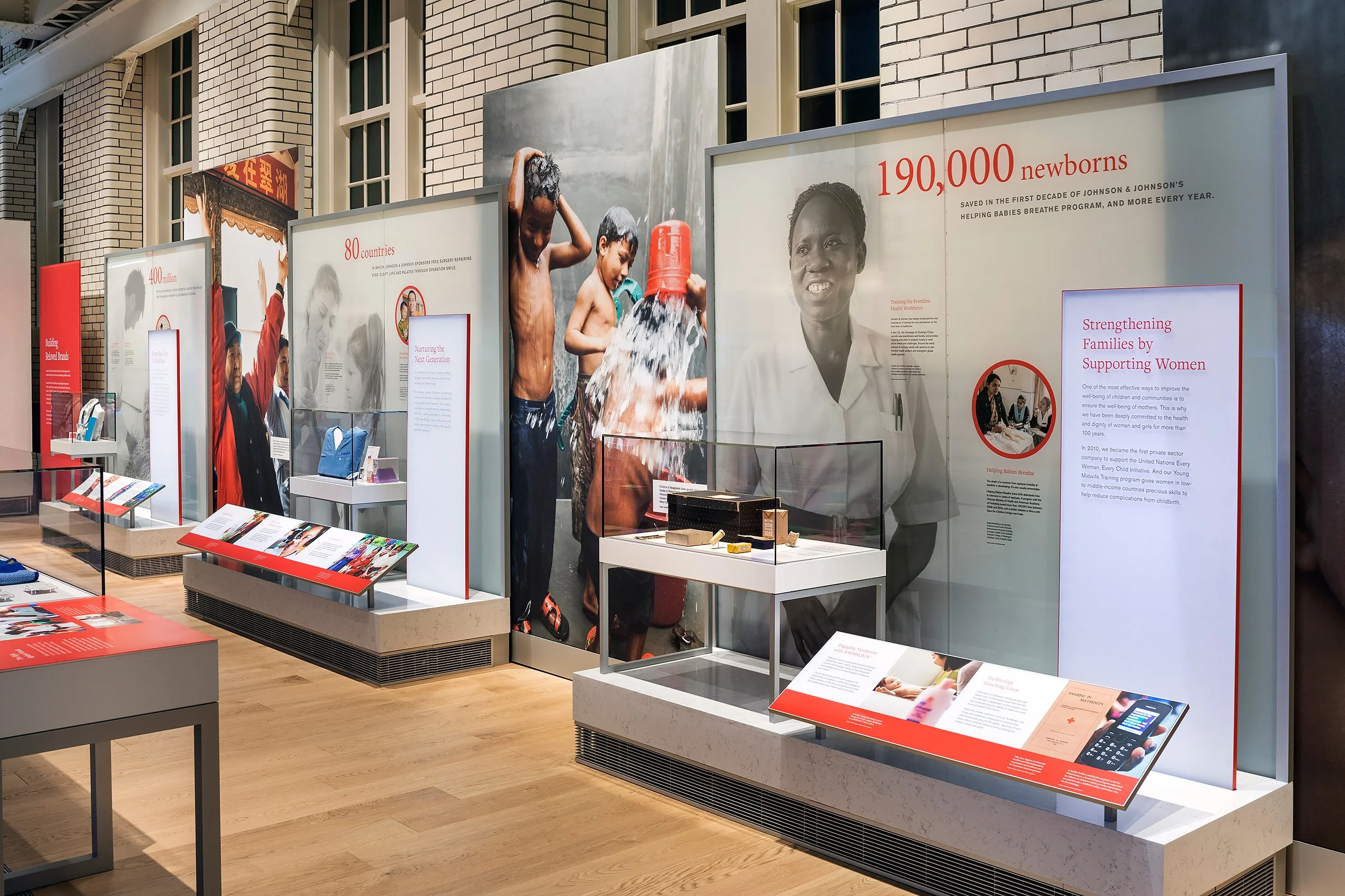Exhibition display panels with information and images about global health initiatives, featuring a large photo of children washing themselves, and text highlighting the impact of Johnson & Johnson's programs in saving lives and supporting families worldwide.