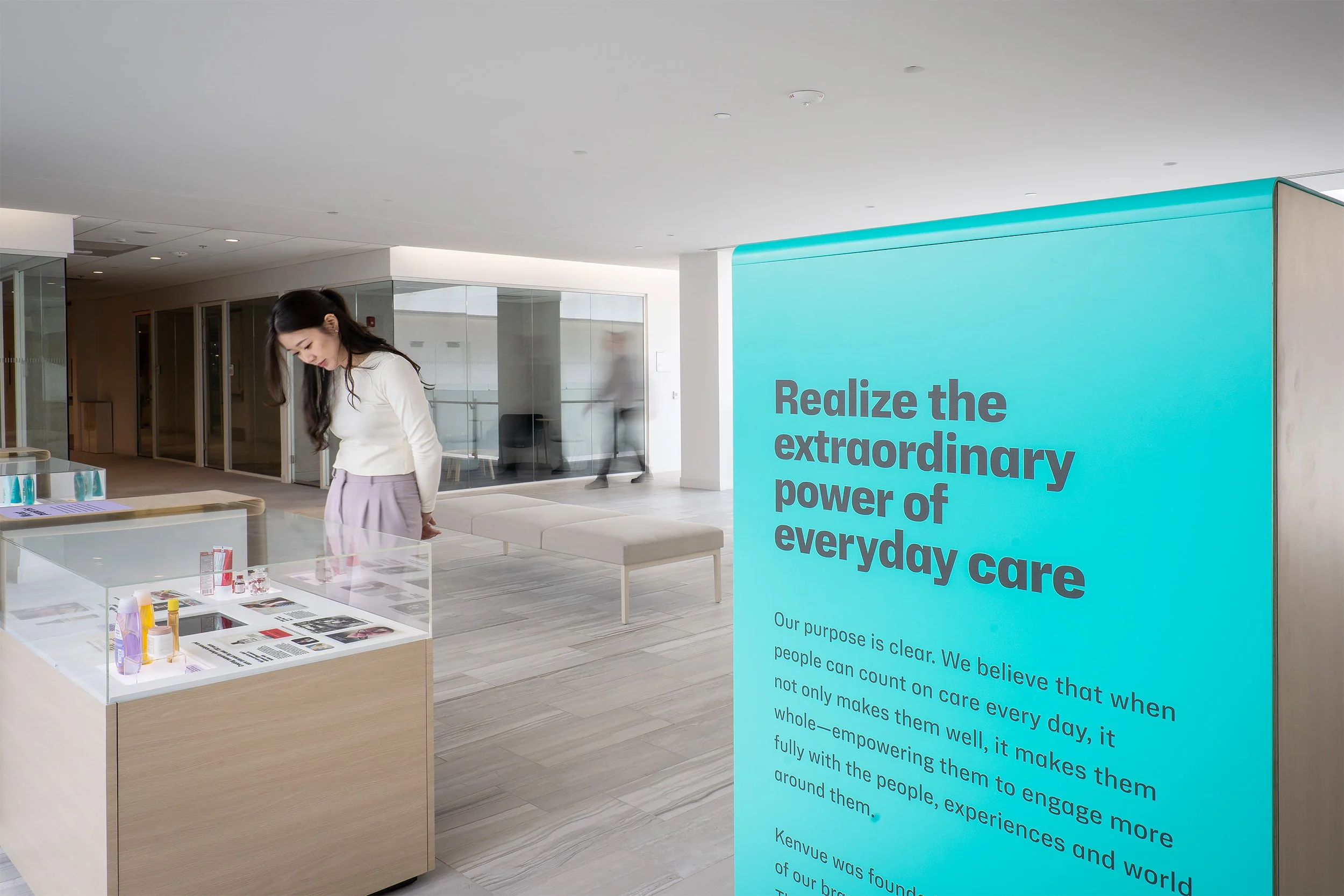 Interior of a modern building with a woman looking at display table and a large blue room divider with text about care and empowerment.