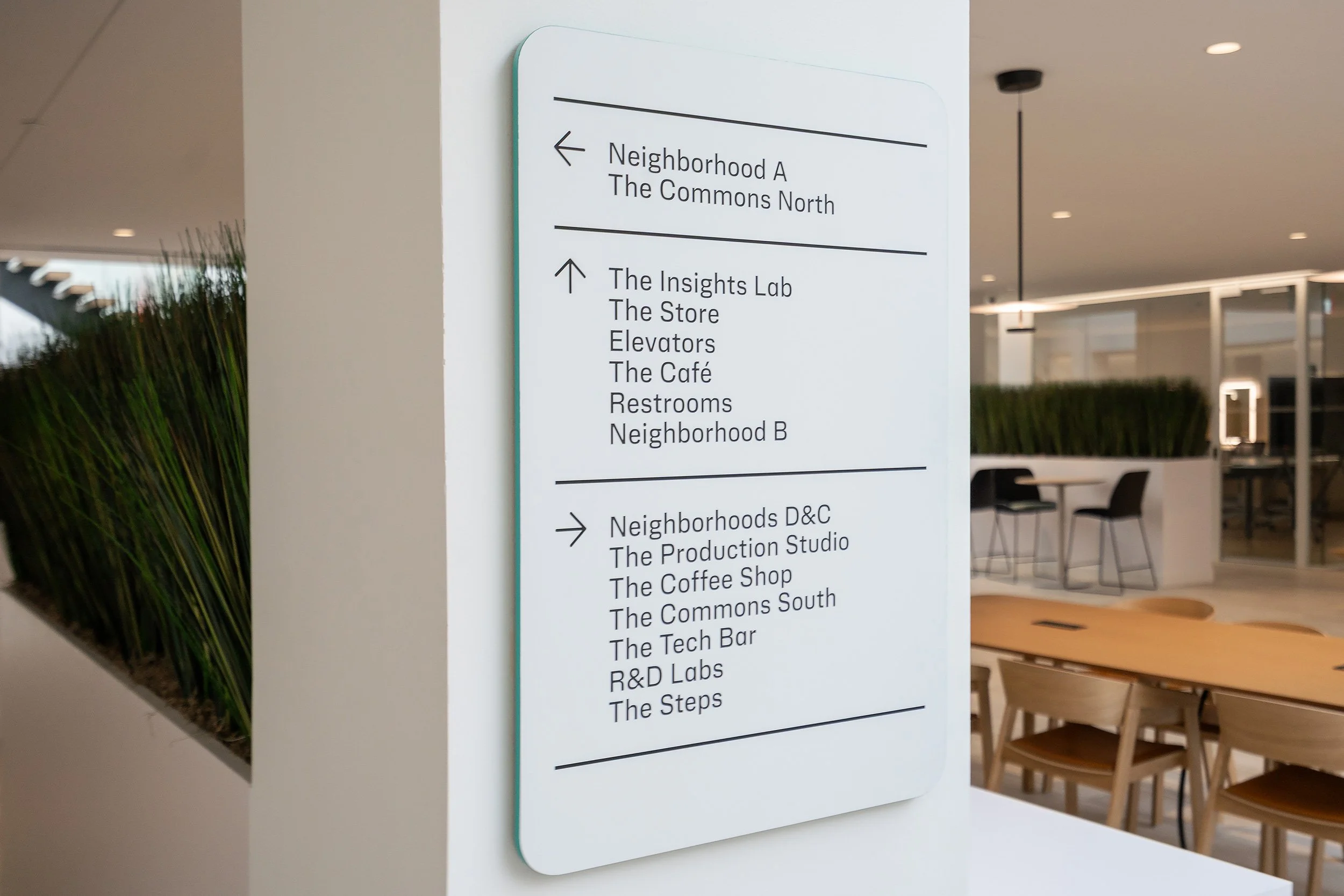 Indoor directory sign listing various neighborhoods and facilities, with directional arrows, in a modern building.