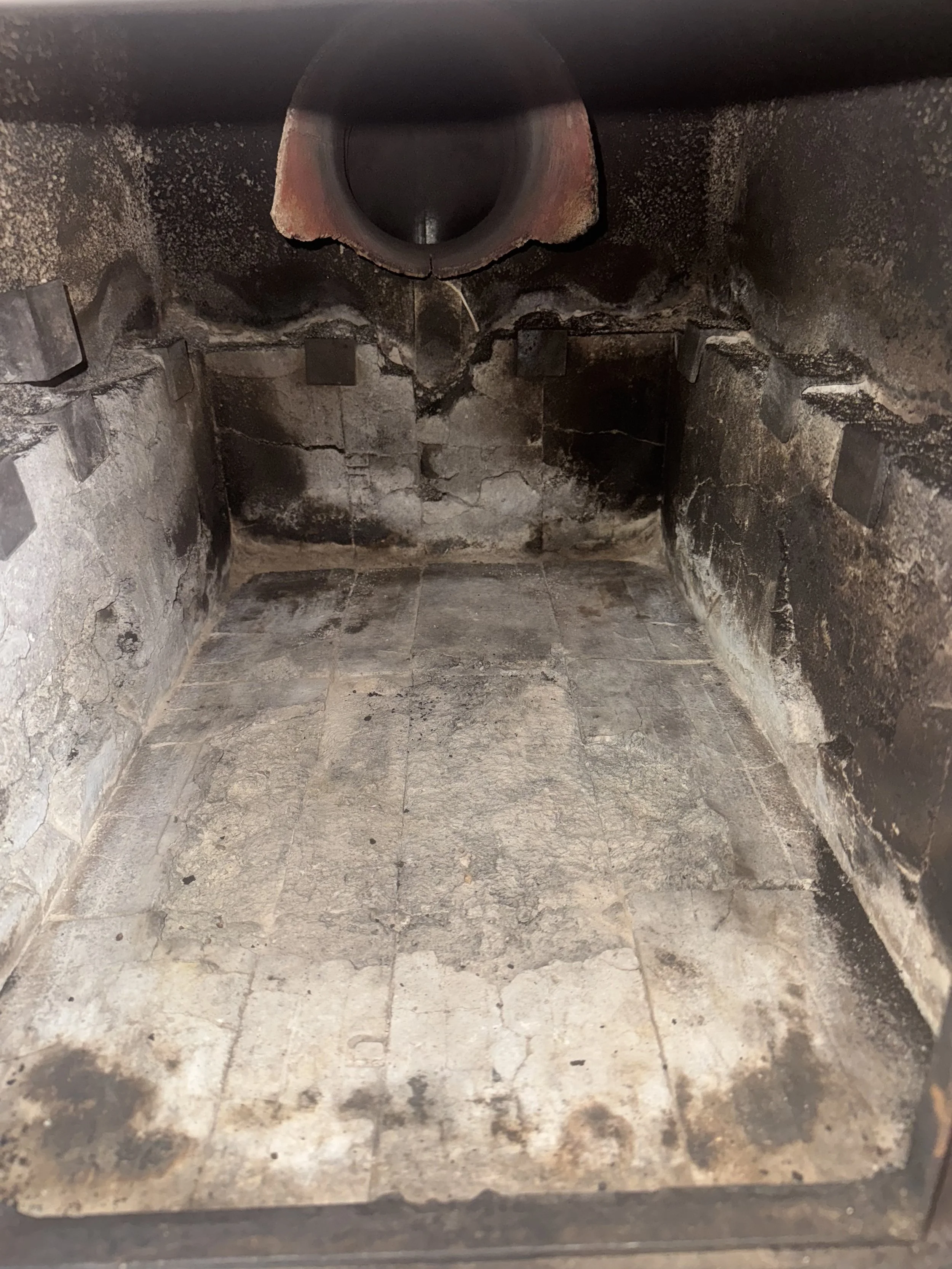 Inside of a dirty, burnt-out chimney with blackened walls, discolored floor, and a charred interior.