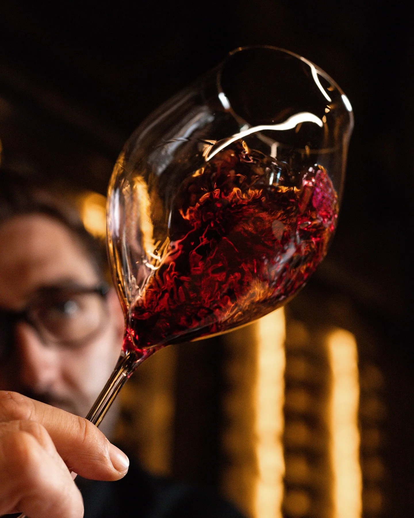 Person holding a glass of red wine, with the wine close up in focus and person slightly blurred in the background.
