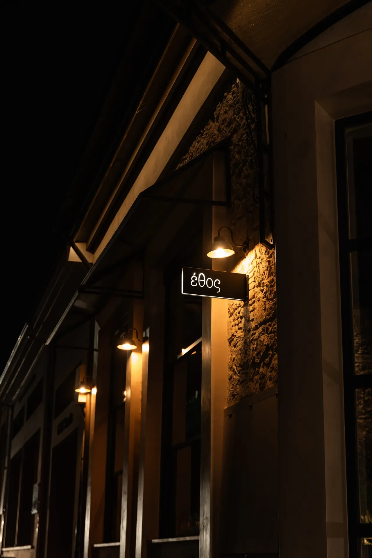 Nighttime photo of a restaurant or cafe exterior with a modern design, warm lighting, and a hanging sign displaying the number 5043
