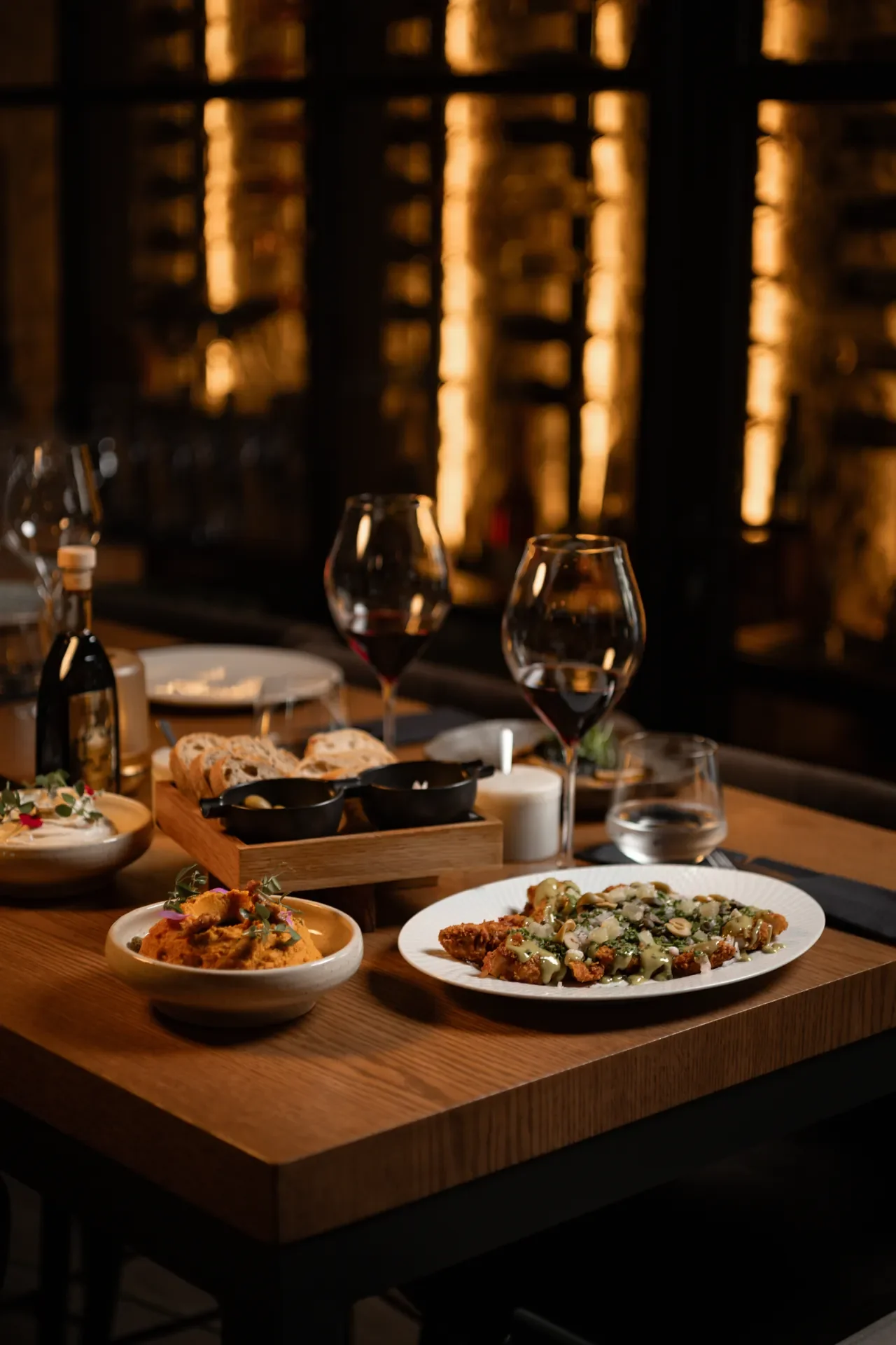 A dinner table with wine glasses, bread, dips, and appetizer dishes in a dimly lit restaurant.