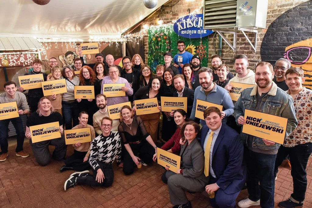 Smiling crowd of folks holding Nick rally signs