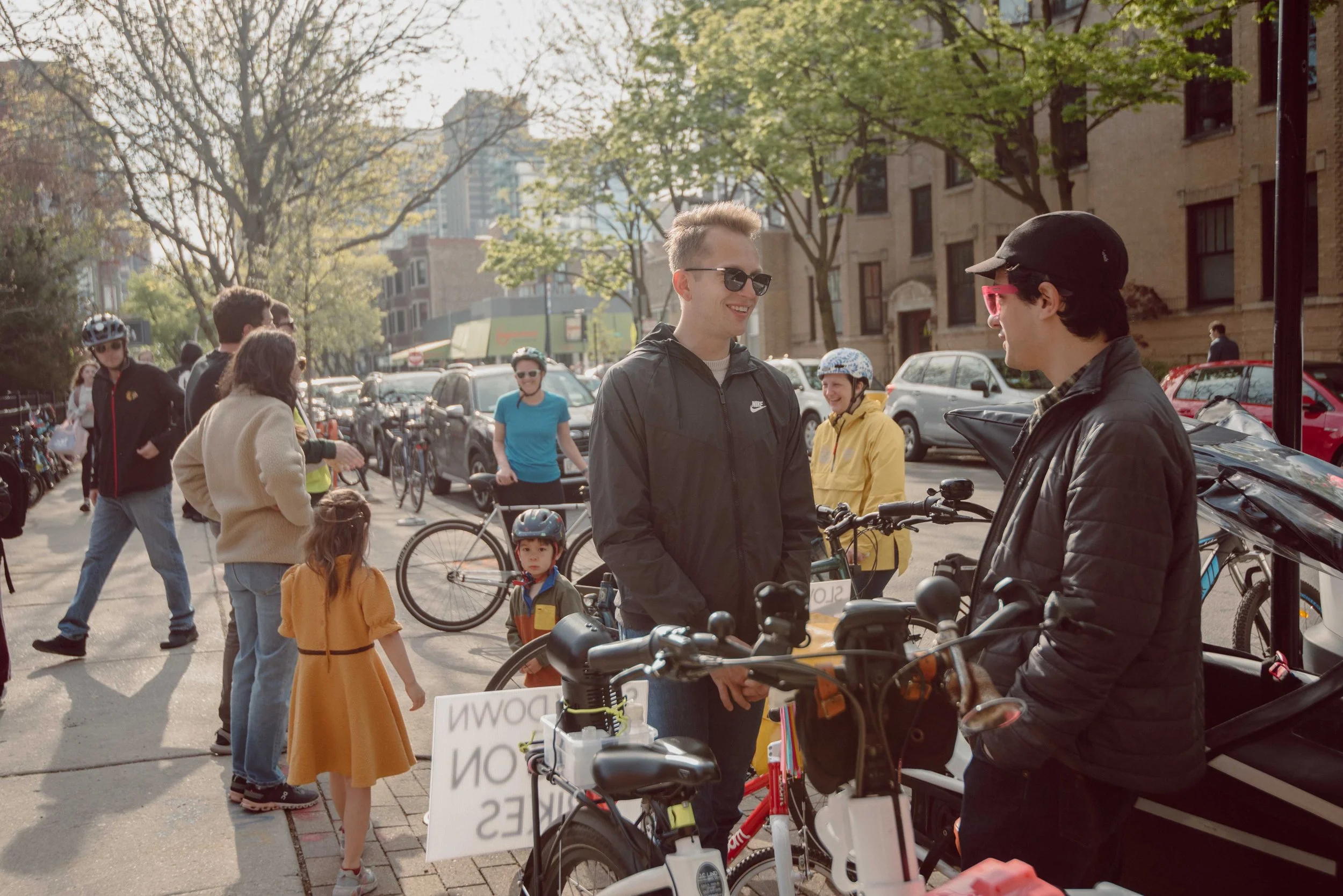 Nick speaks to someone on the street. There is a crowd nearby and most people have bikes.