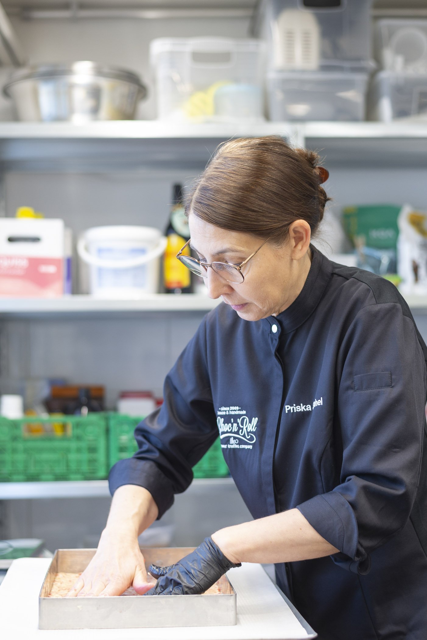 Frau in schwarzer Berufskleidung arbeitet in einer professionellen Küche mit einem Backrahmen, umgeben von Küchengeräten und Zutaten.