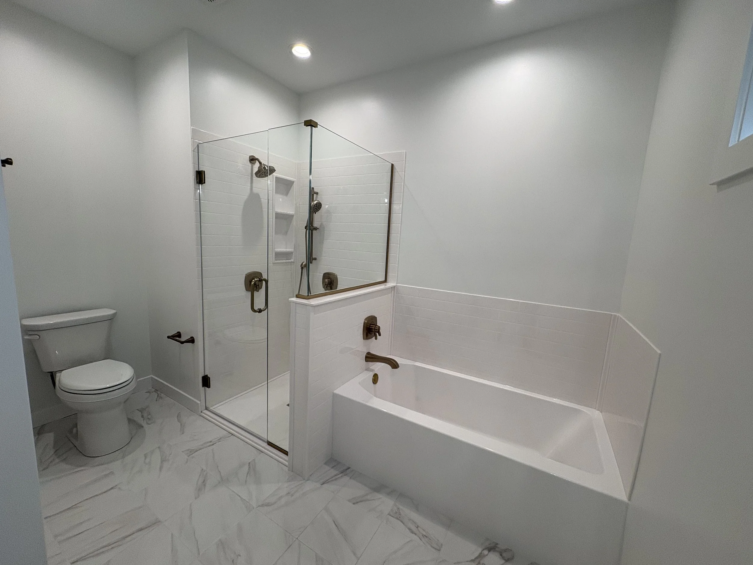 A modern bathroom with a toilet, a glass-enclosed shower with white tiled walls, a bathtub, and white marble flooring.