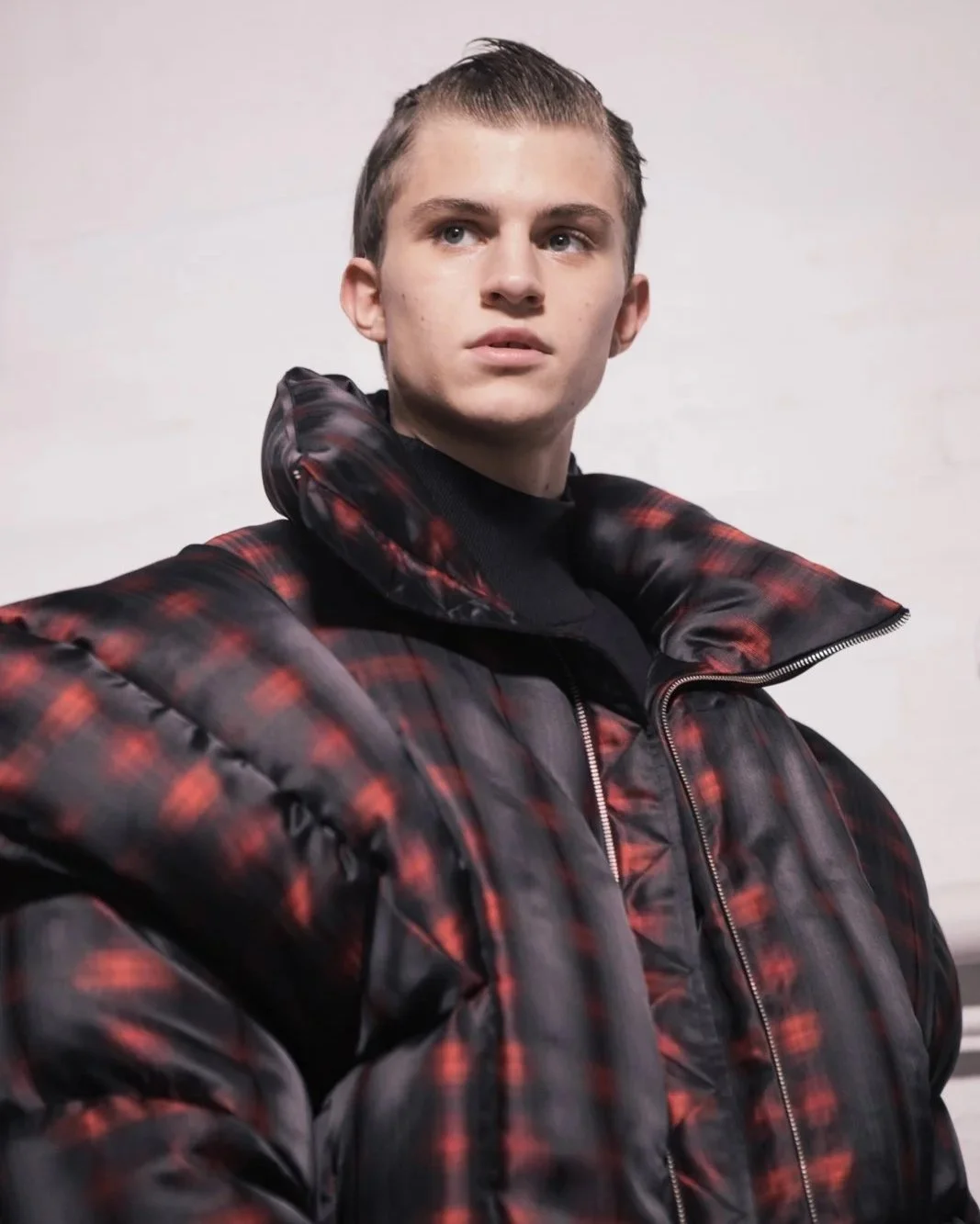 Person wearing a red and black checkered puffer jacket with high collar.
