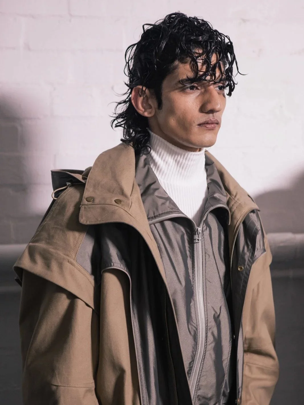 Model wearing layered outfit with beige coat and white turtleneck.