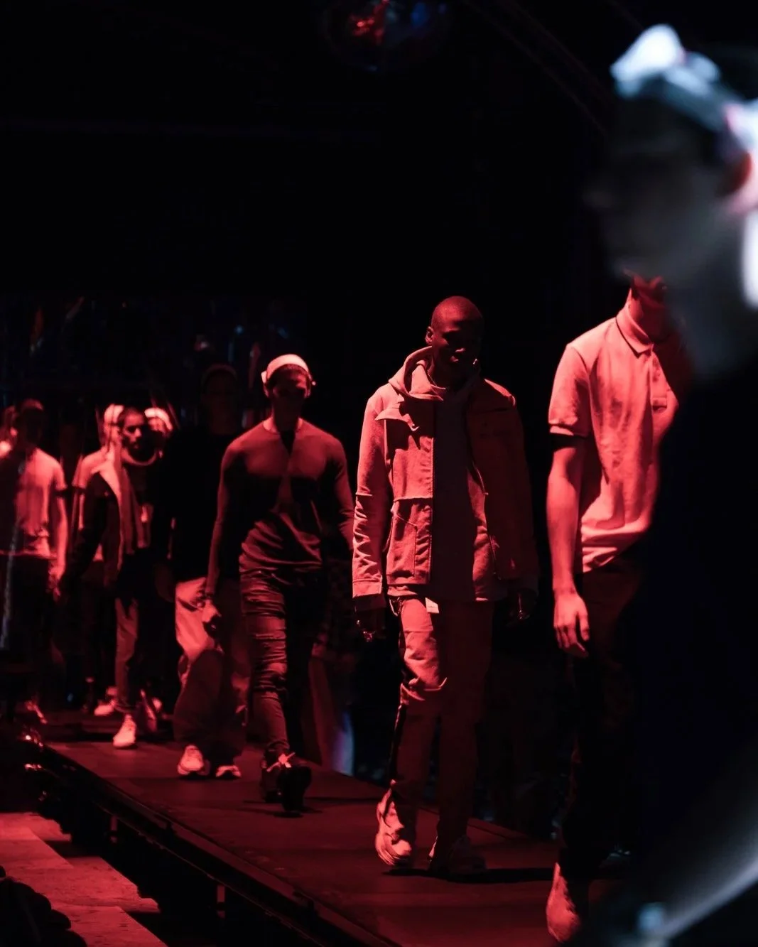 Models walking on a dimly lit fashion runway with red lighting.