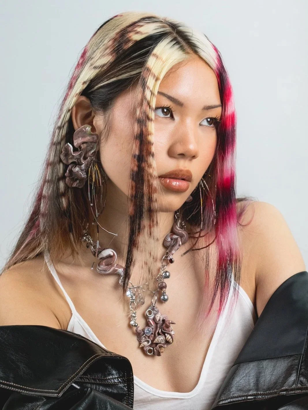 Fashionable woman with colorful, patterned hair, wearing unique jewelry and a leather jacket.