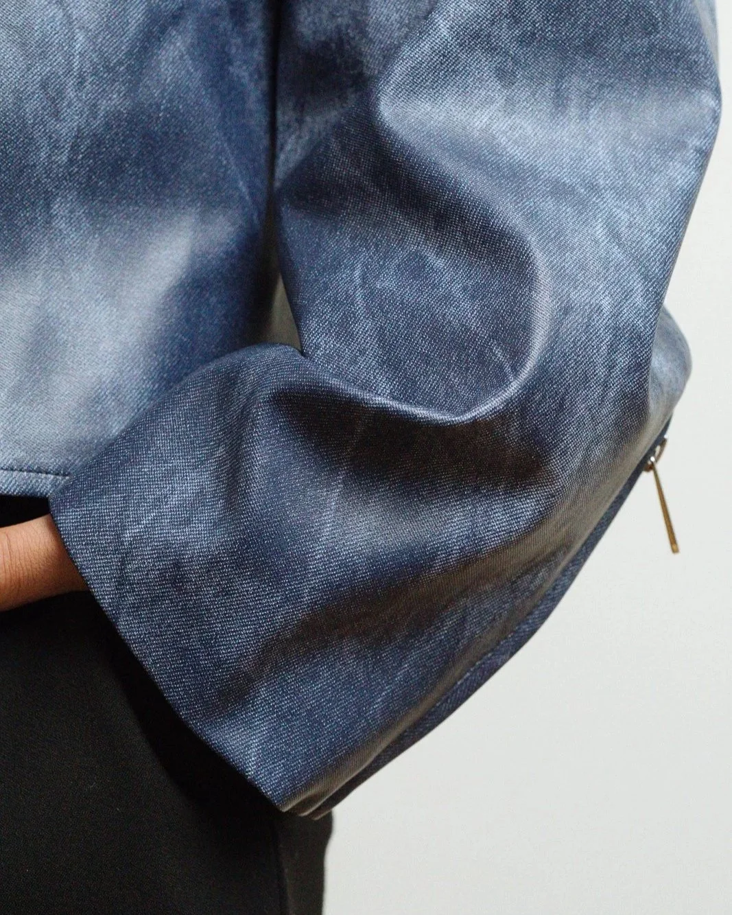 Close-up of a blue denim jacket sleeve with a zipper detail.