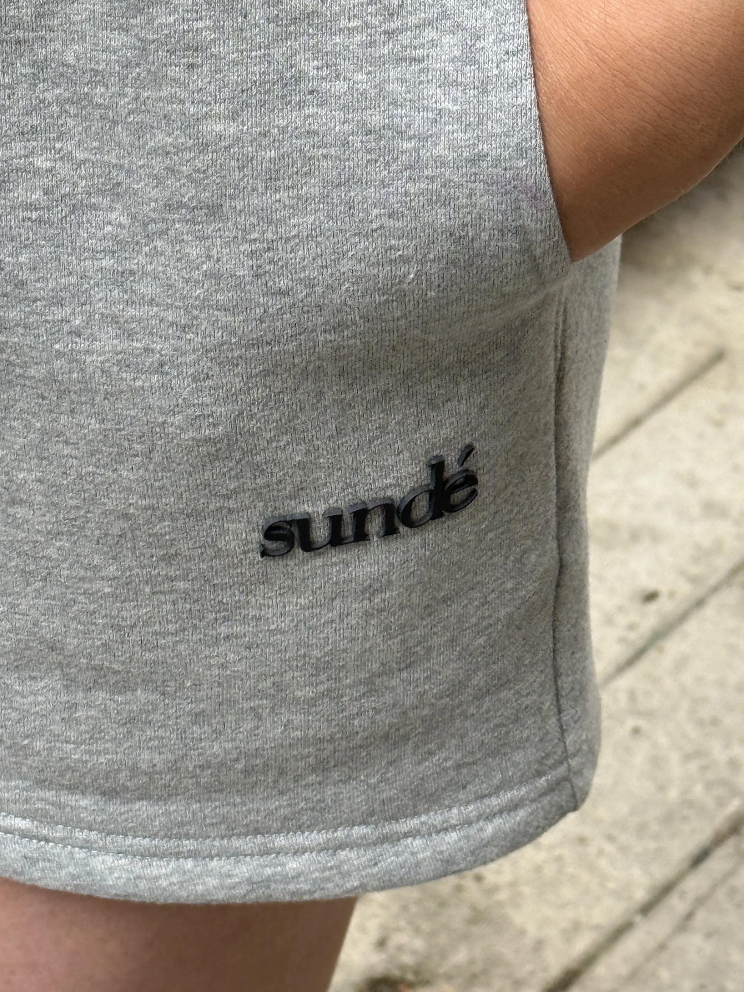 Close-up of a person wearing a grey garment with the brand name 'sundé' in black letters on the fabric.