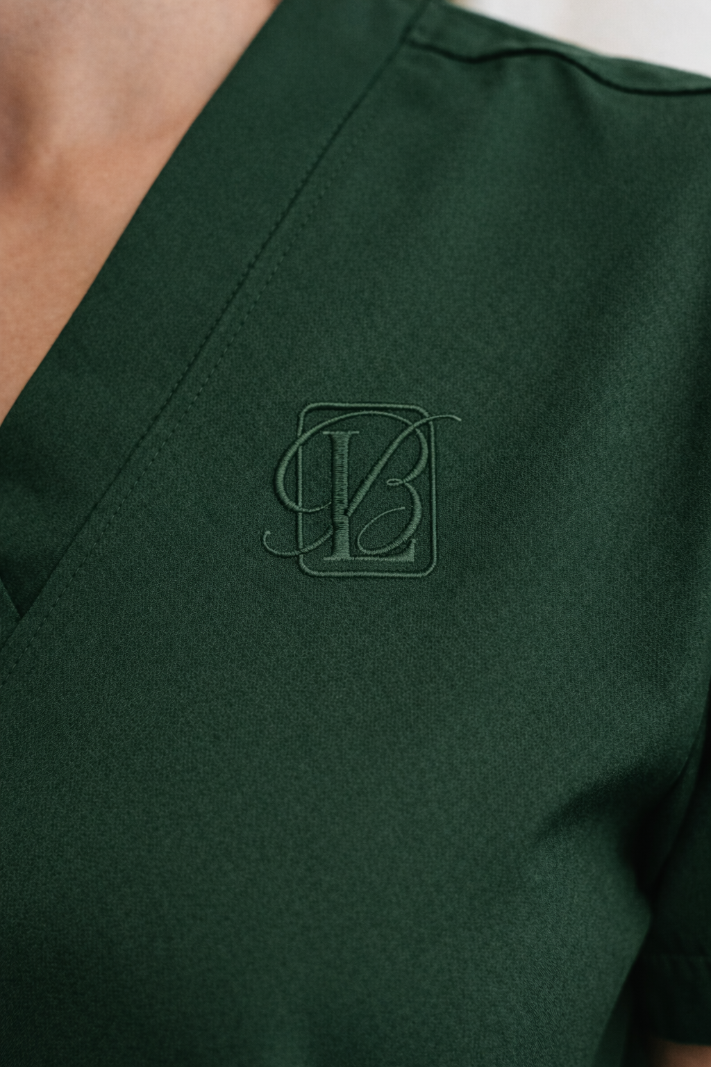 Close-up of a dark green fabric with embroidered monogram 'Y' and 'B' inside a rectangular frame, likely part of a uniform or branded clothing.