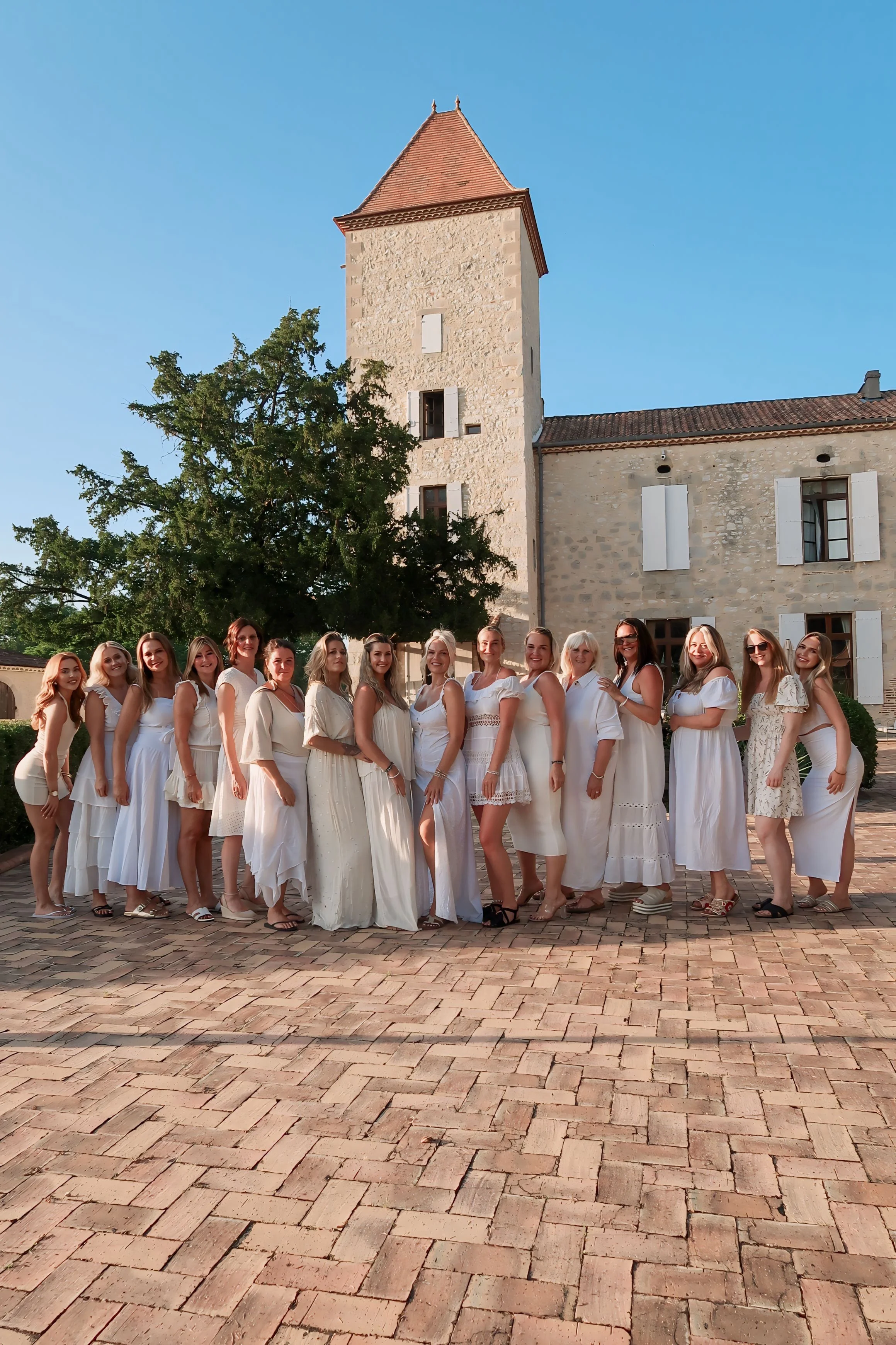 Group of women in white dresses standing in front of a stone building with a tower during daytime.