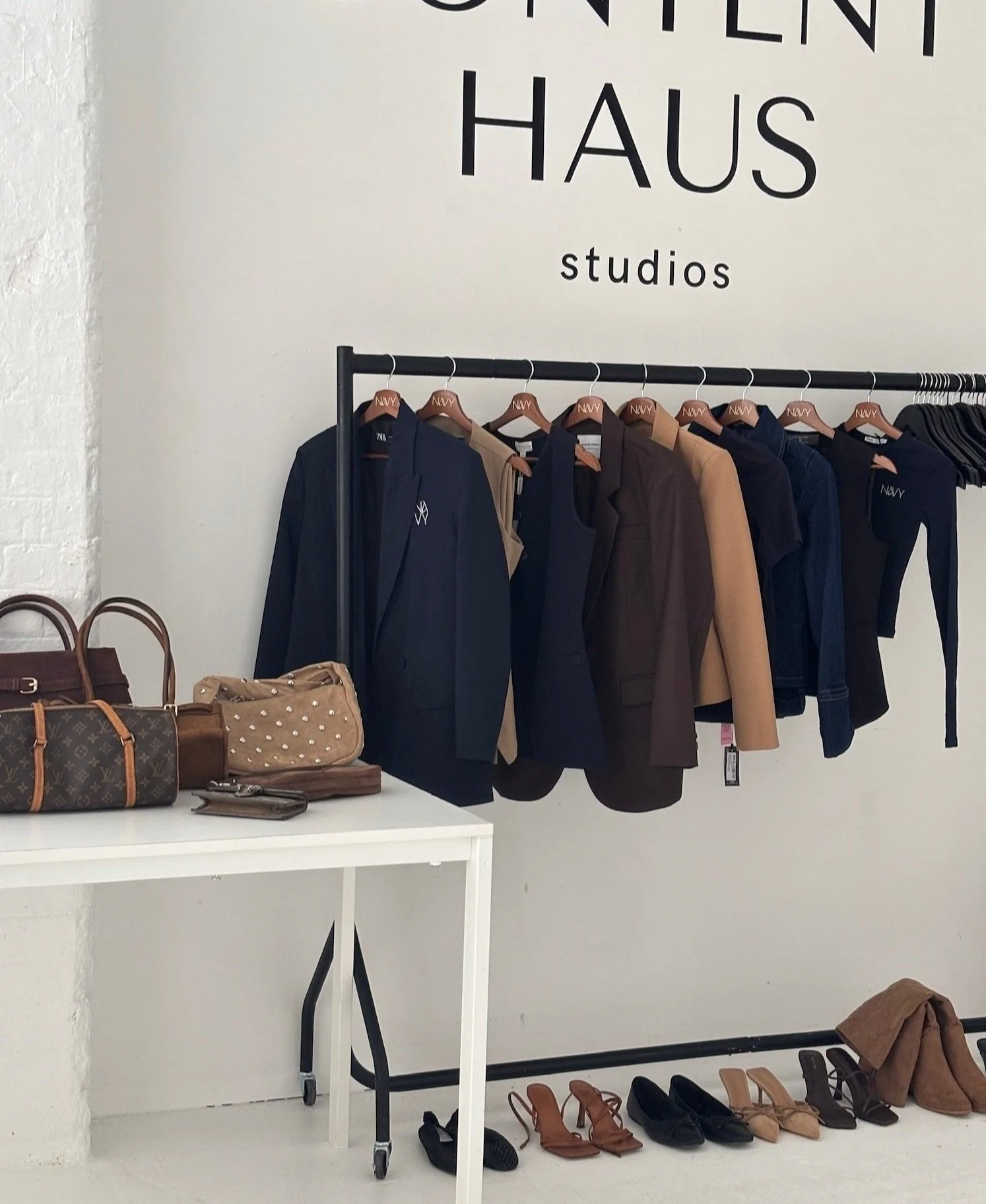 Clothing rack with blazers and jackets, handbags and shoes displayed below, inside a studio with a sign reading 'Content Haus studios'.