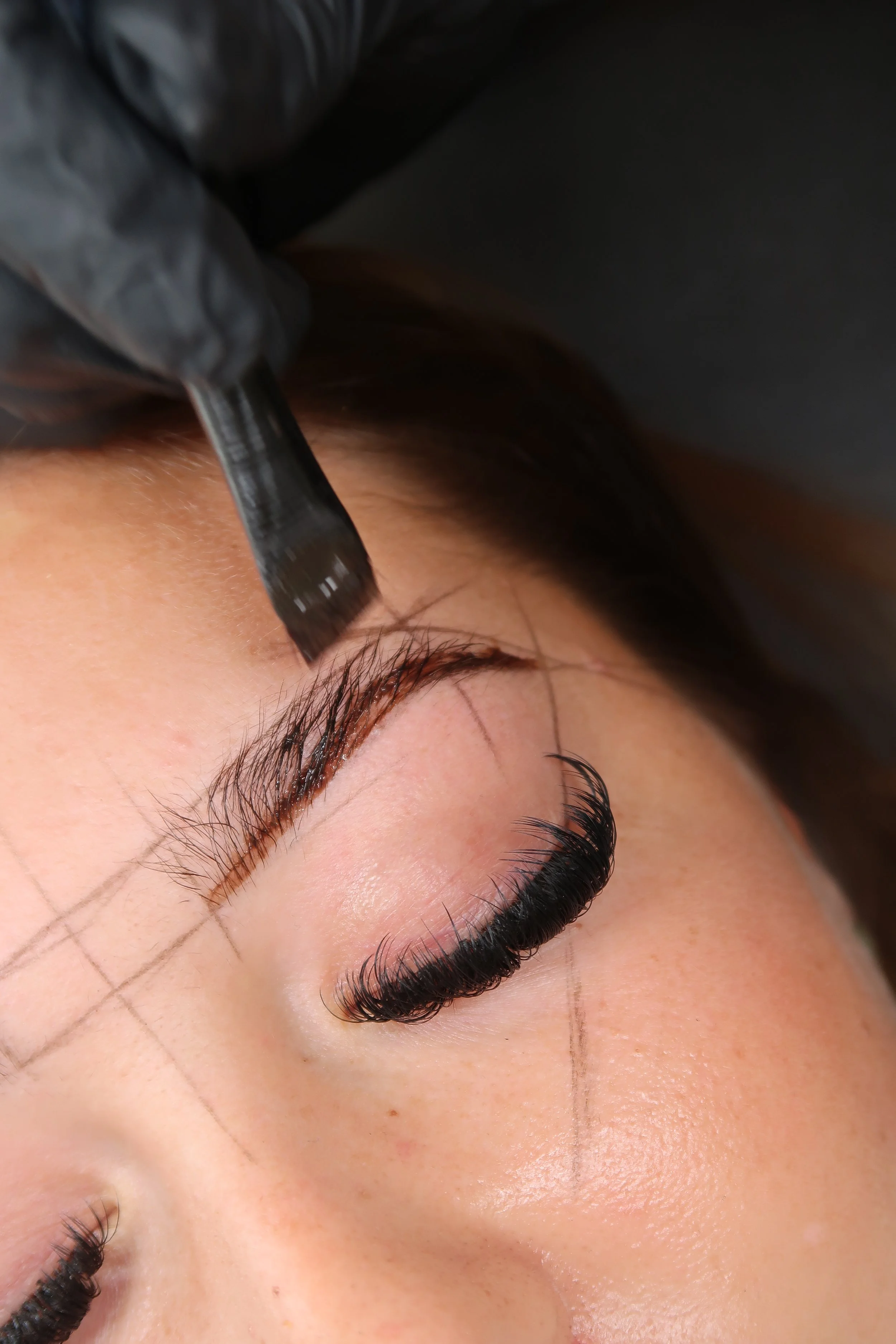 Person receiving eyelash extensions, with markings on the eyelid for precise application.