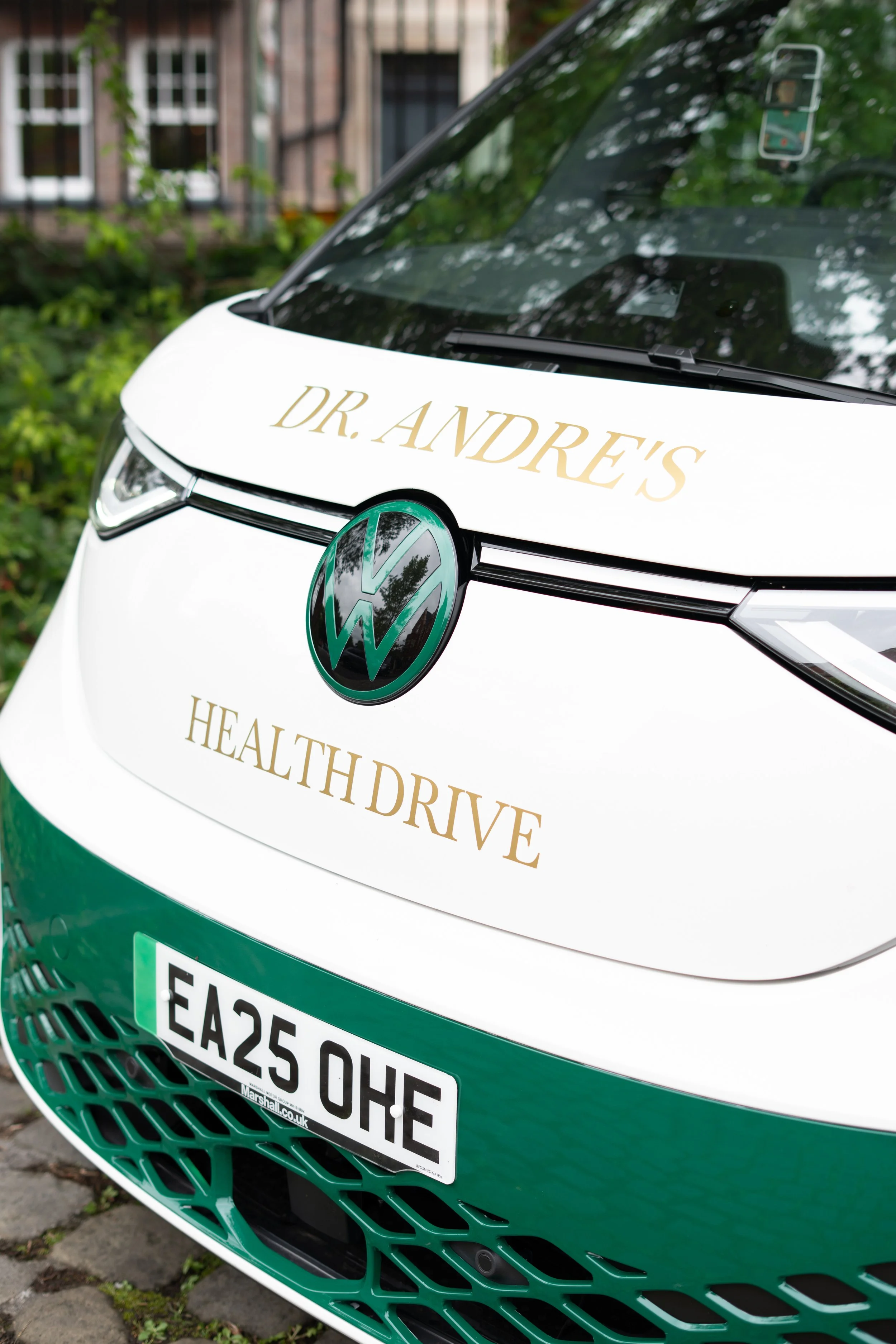 Close-up of a white and green electric vehicle with a Volkswagen logo, displaying the text 'DR. ANDRE'S HEALTH DRIVE' on the front.