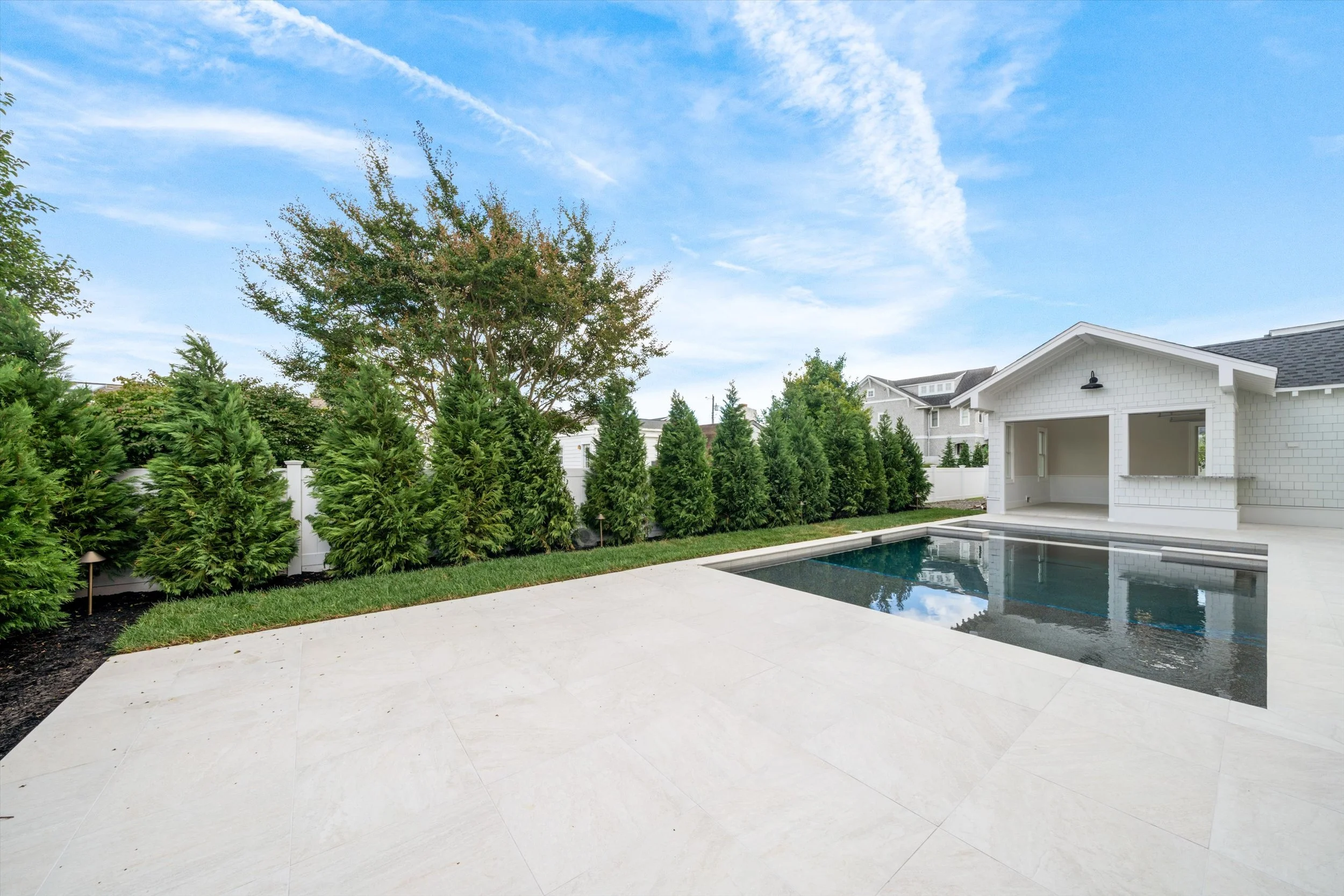 Porcelain paver patio beside the pool, framed by evergreen privacy trees, 245 57th St, Avalon, NJ