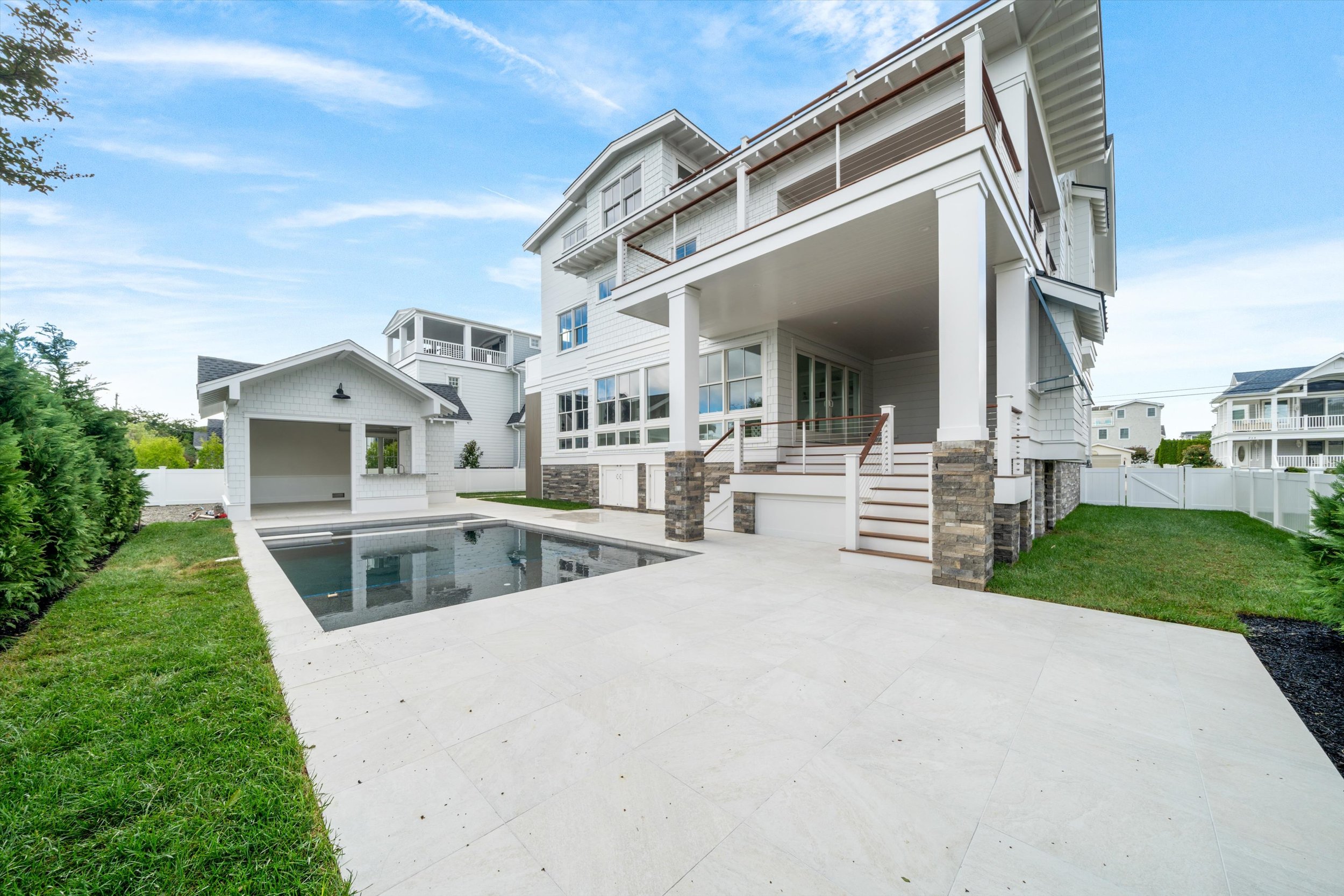 Rear of a new custom home with covered porches, a gunite pool and a pool cabana, built by Coastal Modern Construction at 245 57th St, Avalon, NJ