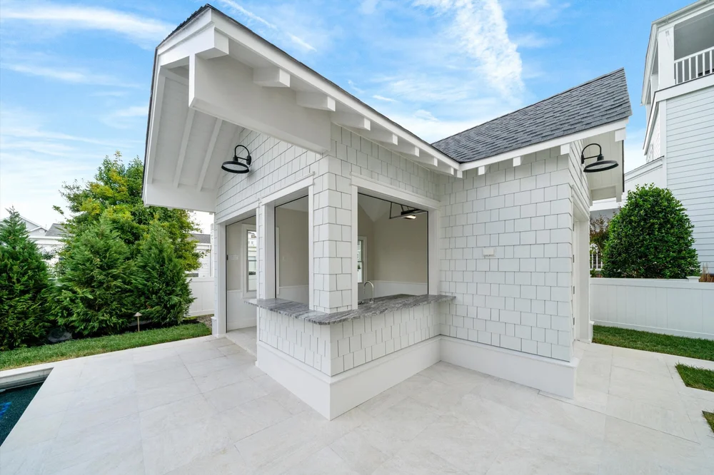 Custom pool house with outdoor bar and stone patio beside a pool, built by Coastal Modern Construction