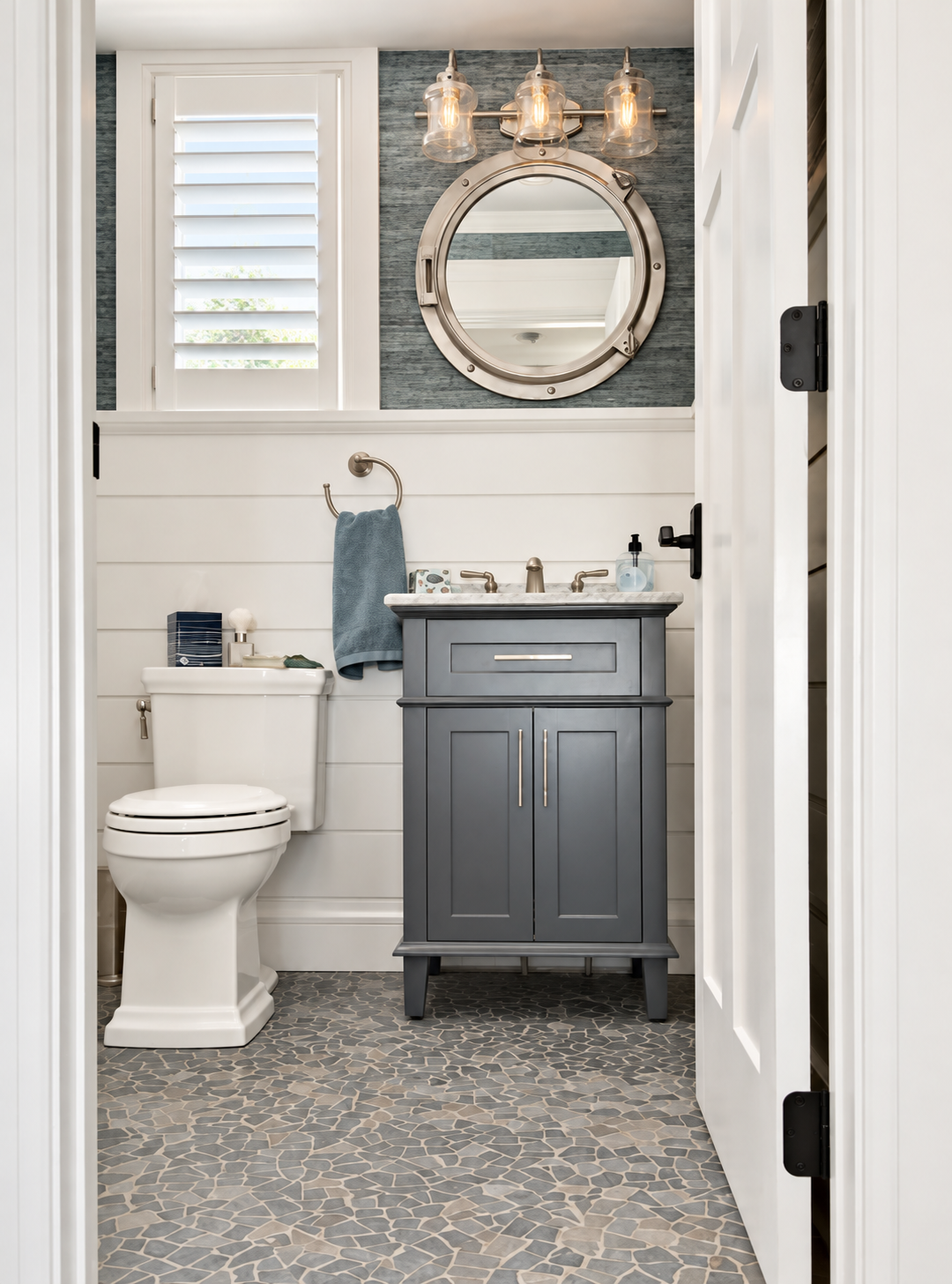 Powder room with a porthole mirror, gray vanity and shiplap walls in the renovated Sea Isle City duplex