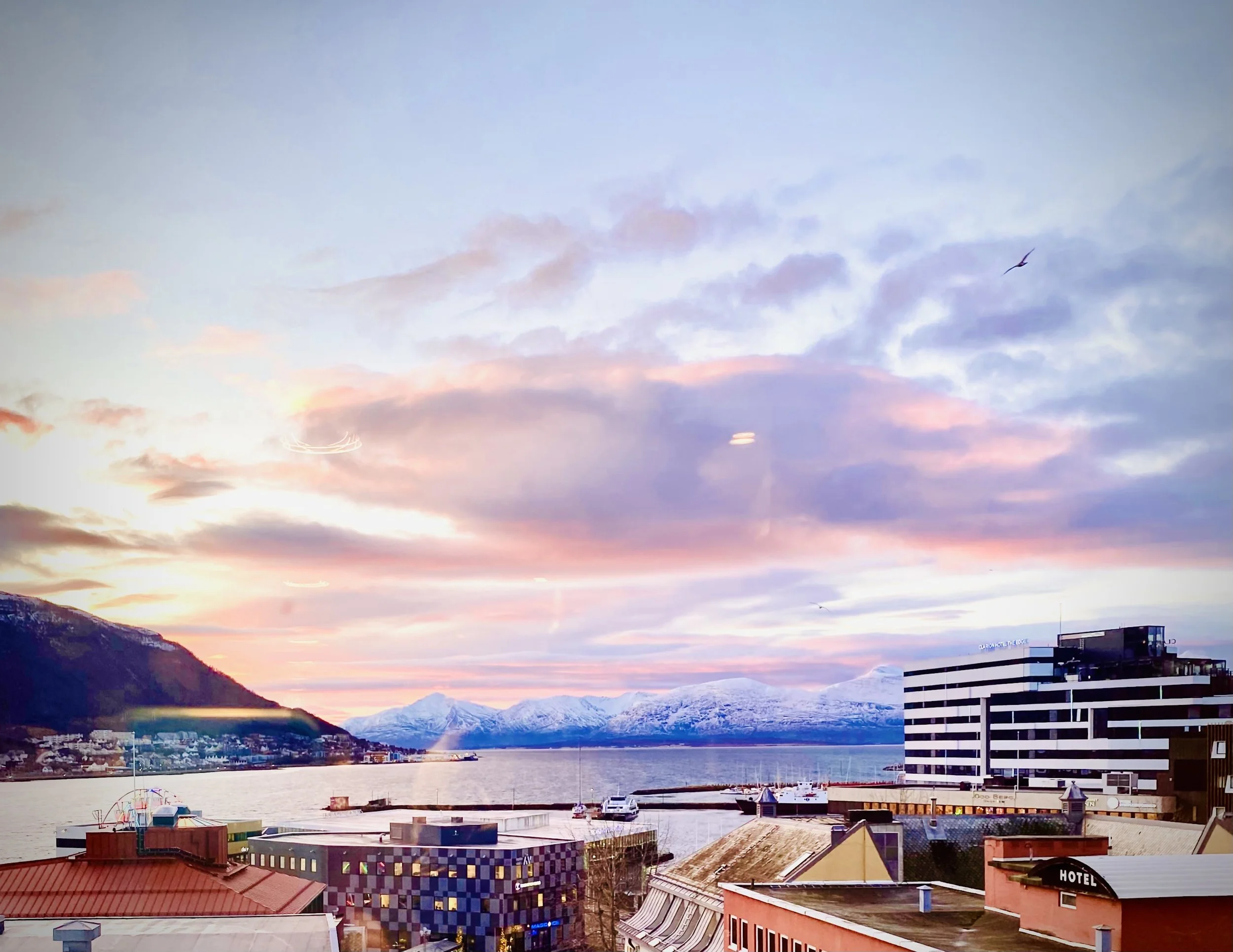 Coastal cityscape at sunset with mountains in the background, water, boats, and modern buildings in the foreground. Scenic scenery, sunrise , the space between night and day
