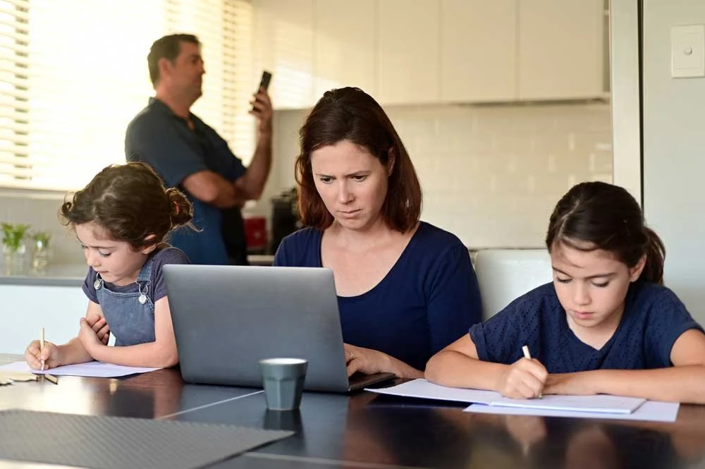 Woman trying to work from home in her busy kitchen with her husband and daughters working around her.