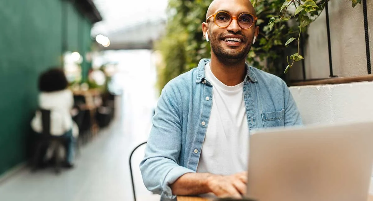 Tall happy guy sat smilling optimistically from his outdoor table and Macbook